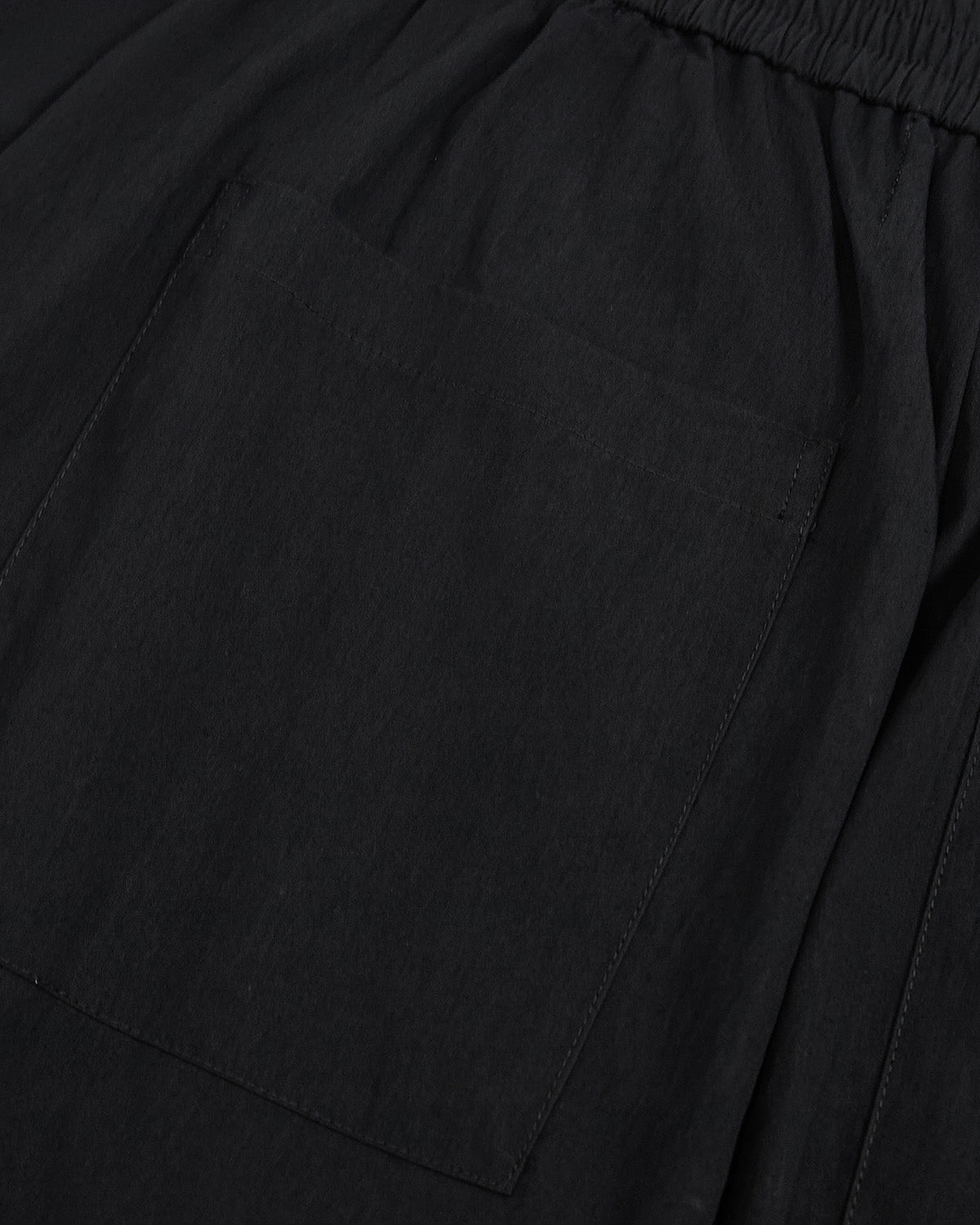 Close-up of black nylon fabric texture and seam construction detail on Sundae School pleated pants