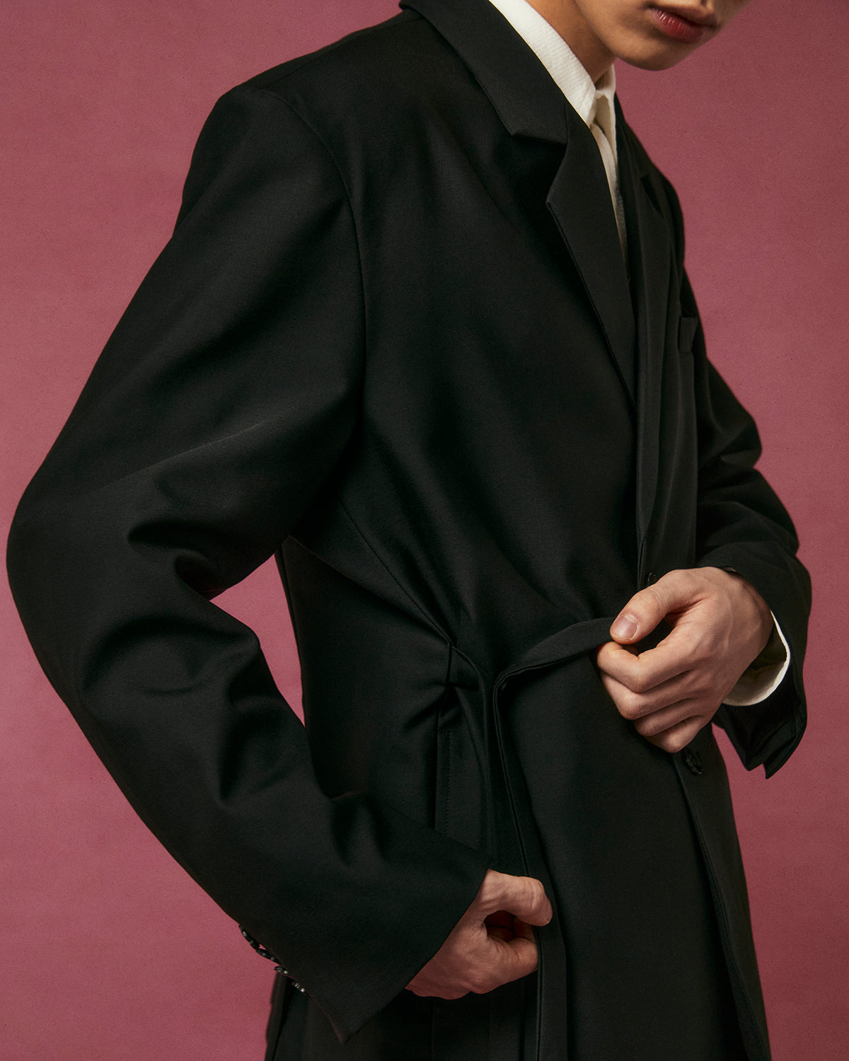 A person adjusts the belt of the Sundae School BLACK DOUBLE DUTY BLAZER at their waist against a pink background, with their face partially out of frame.