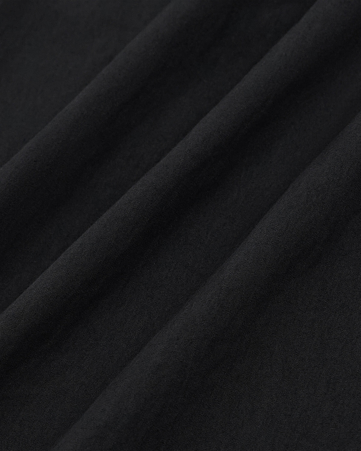 Detail of black nylon fabric drape and texture showing material weight and flow of Sundae School pleated pants
