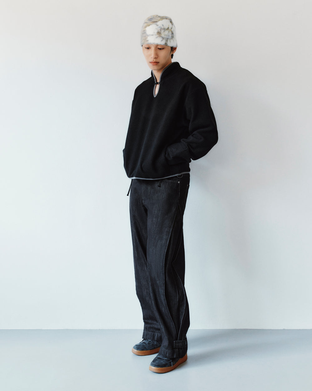 A person wears a black quarter-zip fleece, Sundae School BLACK ACCORDION DENIM PANTS with side pleats, and dark sneakers.