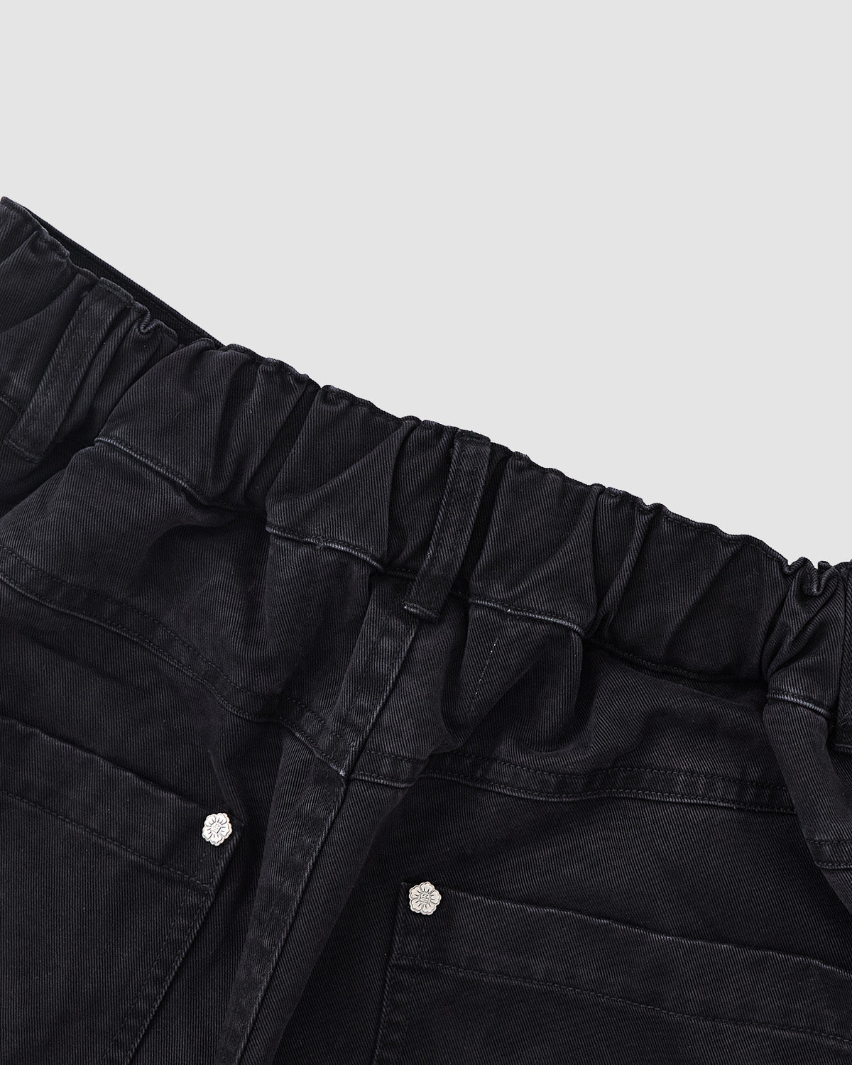 Close-up of the waistband and upper section of Sundae School BLACK ACCORDION CHINO PANTS, featuring an elastic, gathered waistband and visible back pockets, set against a light gray background.