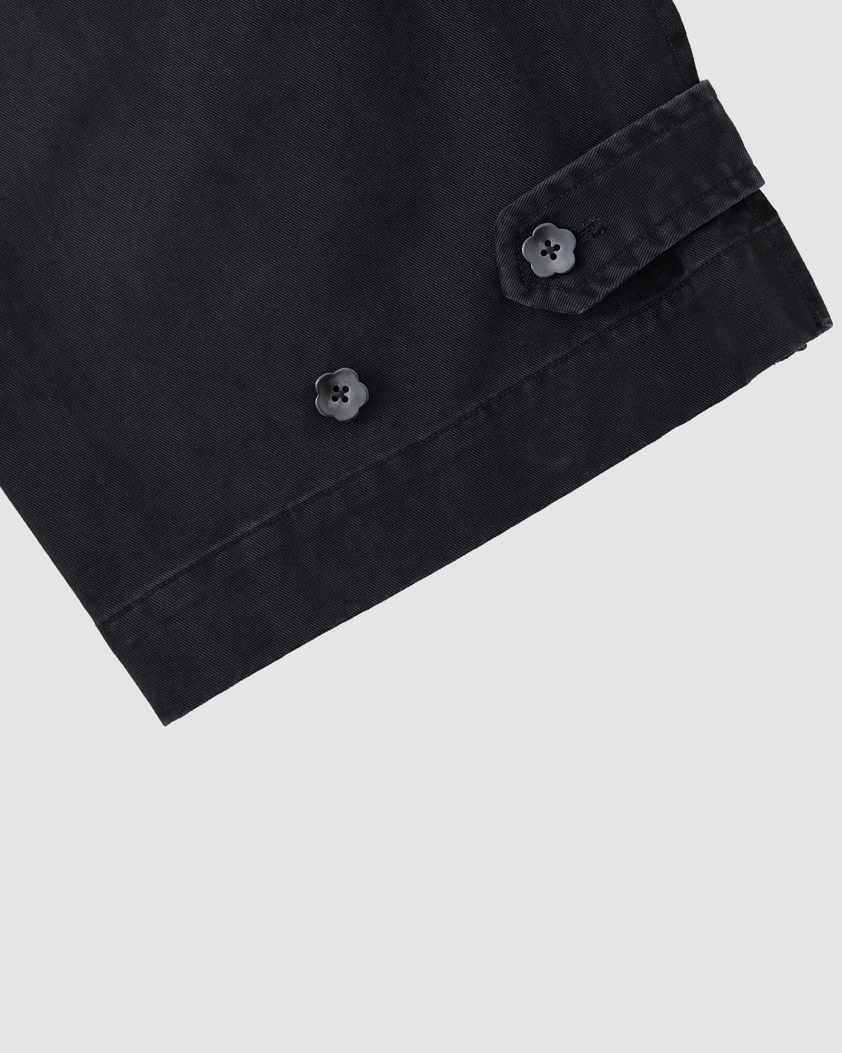 Close-up of Sundae School’s BLACK ACCORDION CHINO PANTS sleeve, featuring two black cuff buttons and hidden accordion pleats, set against a light gray background.