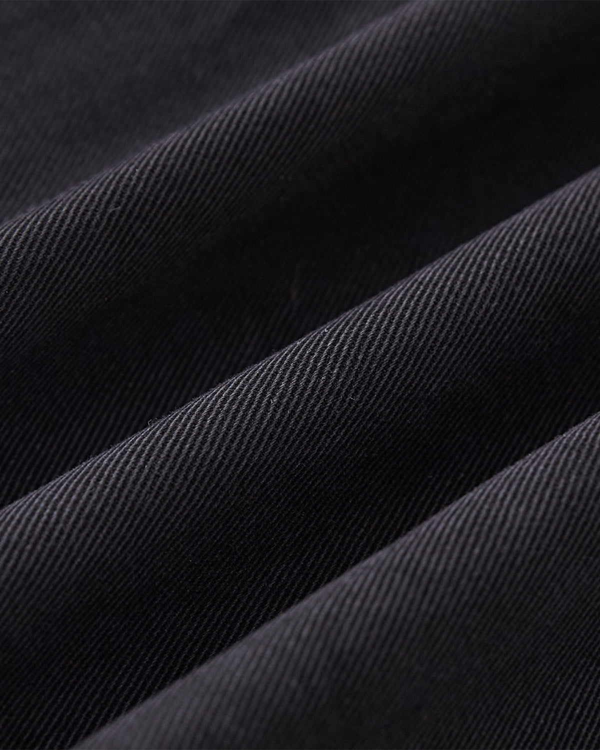 Close-up of BLACK ACCORDION CHINO PANTS by Sundae School—black, ribbed fabric with diagonal textured lines and soft folds, showcasing the sturdy, tightly woven material ideal for unisex wear.