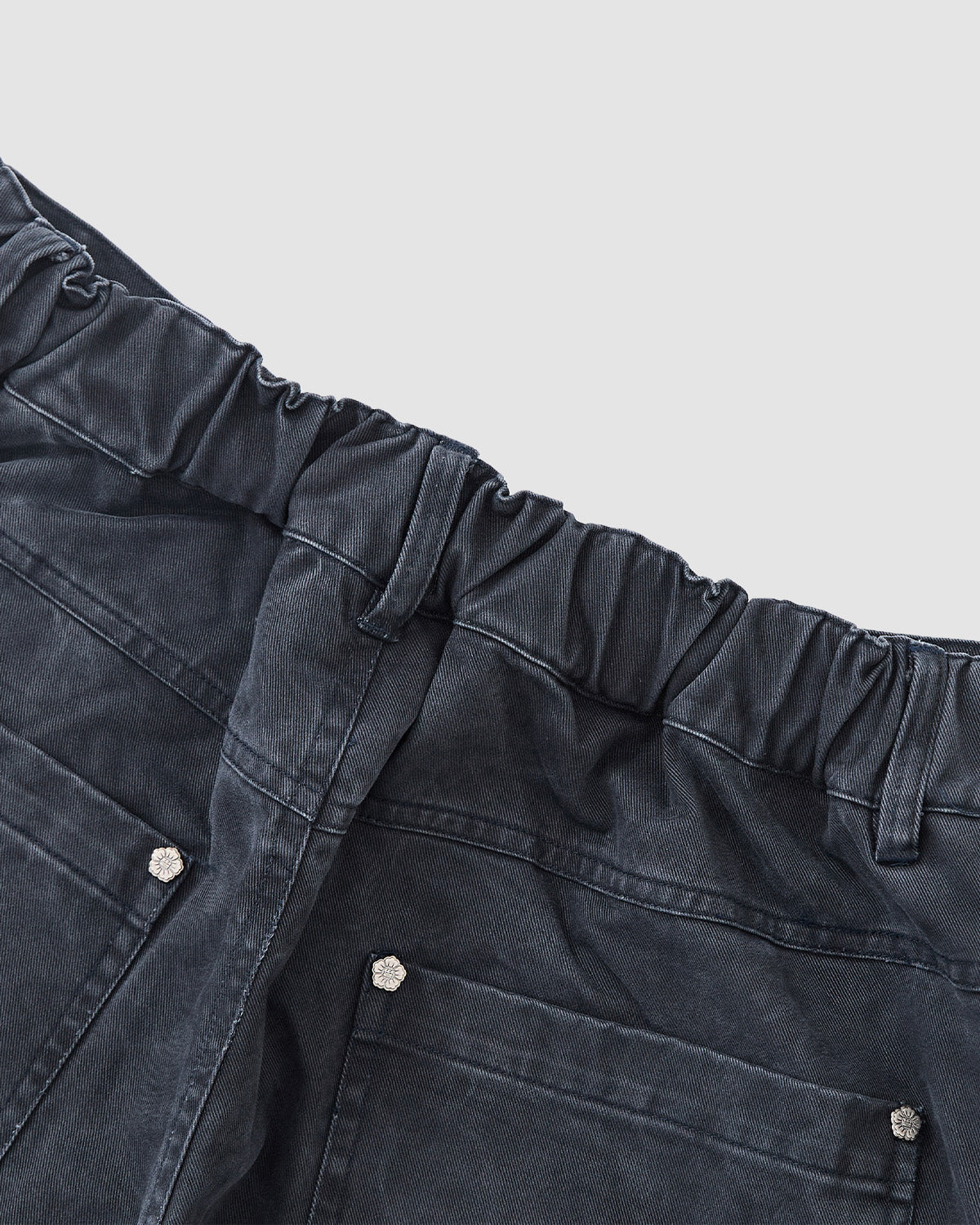 Close-up of the back of Sundae School CHARCOAL ACCORDION CHINO PANTS with an elastic waistband, belt loops, and two large back pockets with silver buttons. The charcoal fabric features a slightly worn look.
