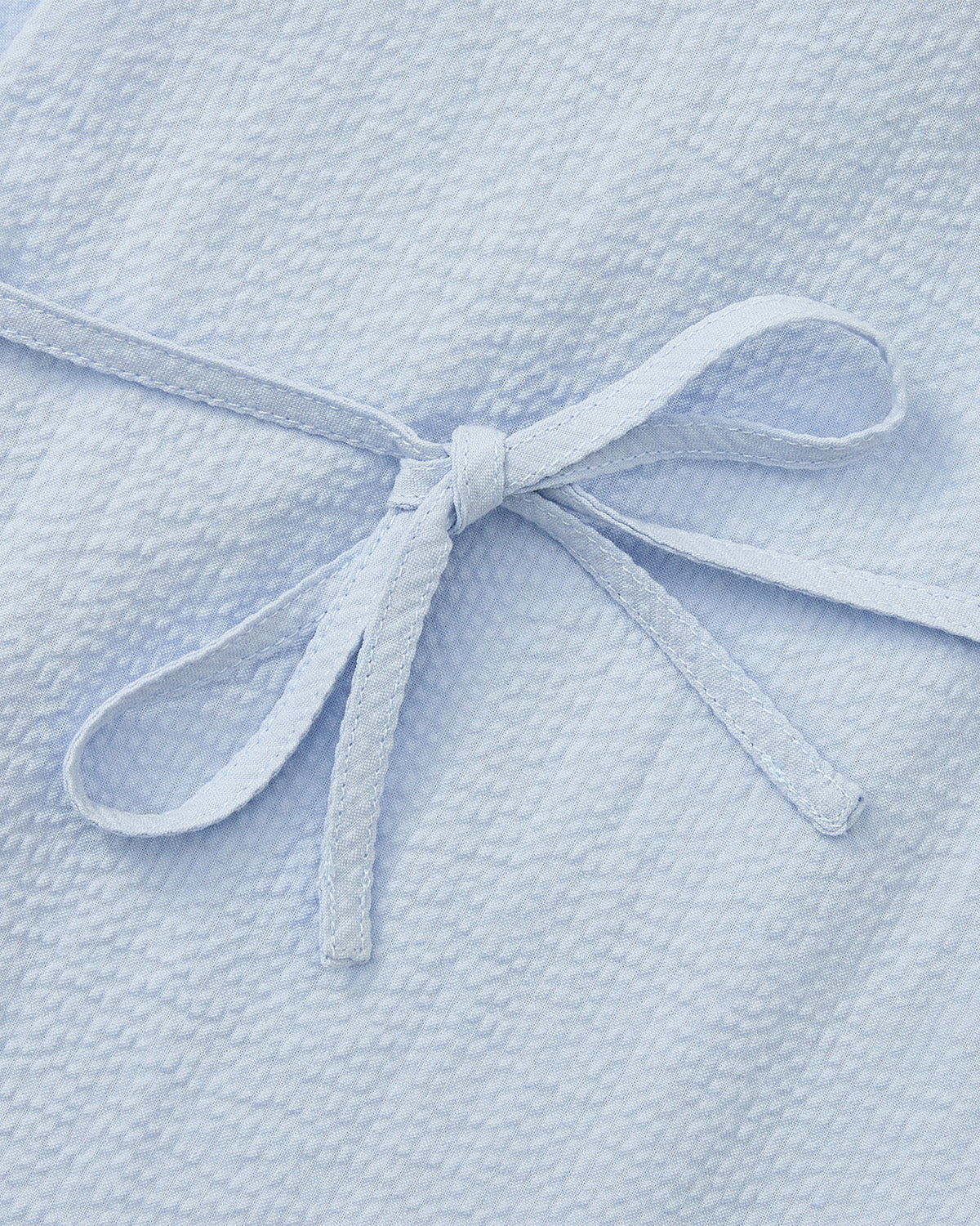 Close-up of the SKY BLUE TIE GORUM SHIRT by Sundae School, featuring textured seersucker cotton and two matching fabric ties forming a bow at the center.
