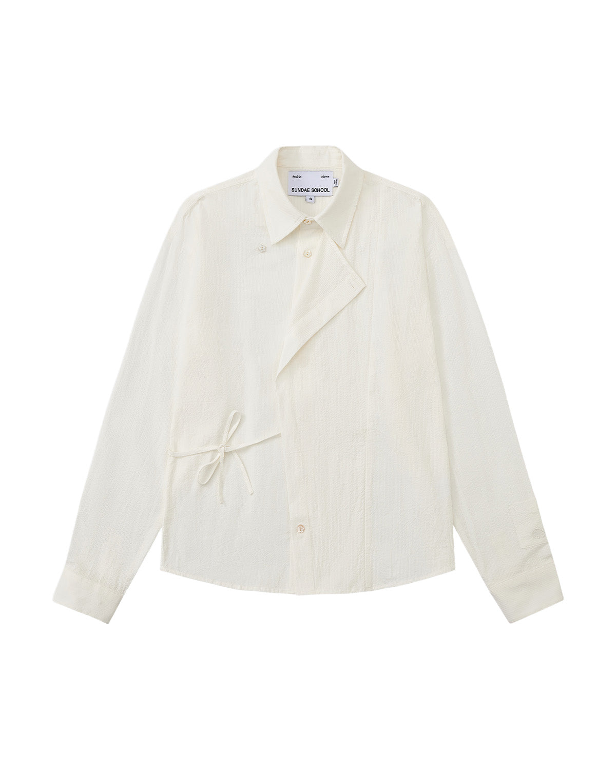A front flat-lay view of an off-white long-sleeve button-up shirt crafted from textured crinkle fabric. It features an asymmetrical wrap-front construction with a side waist tie, a pointed collar, and flower-shaped button details.