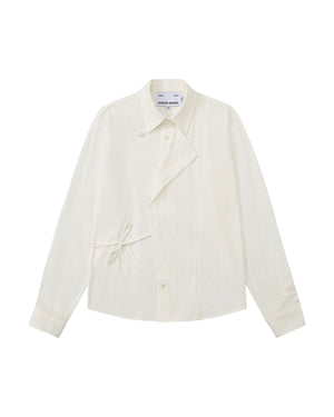 A front flat-lay view of an off-white long-sleeve button-up shirt crafted from textured crinkle fabric. It features an asymmetrical wrap-front construction with a side waist tie, a pointed collar, and flower-shaped button details.
