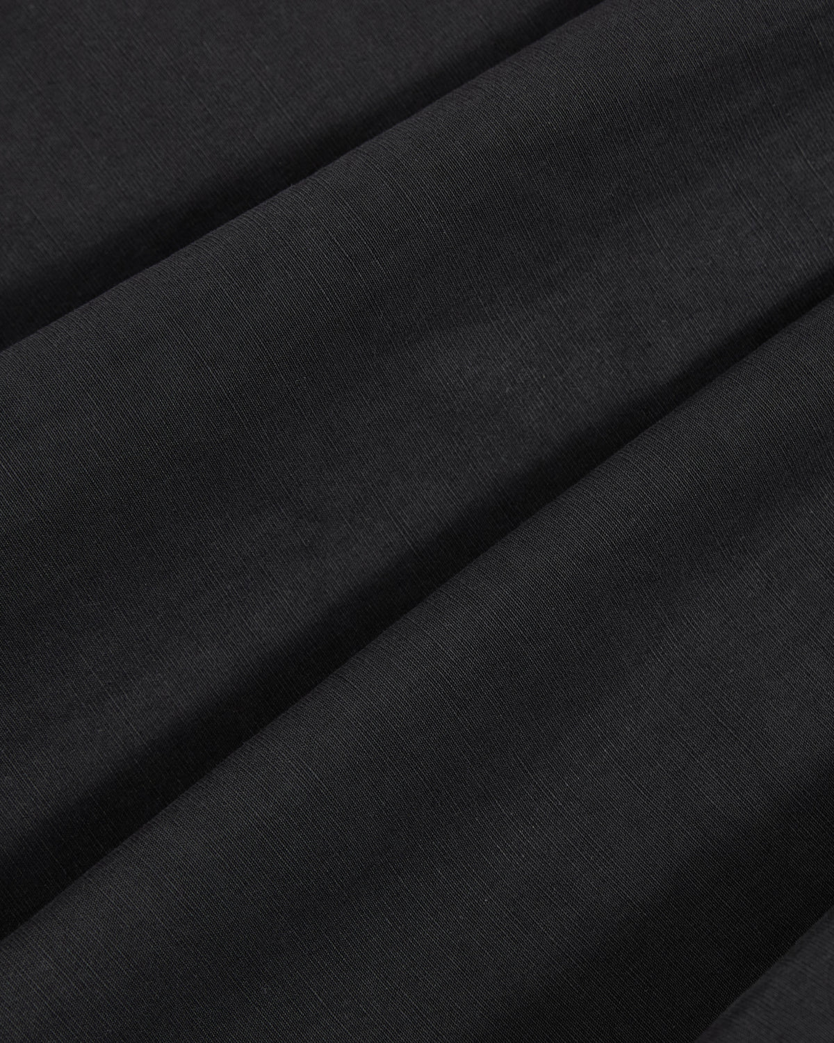 Close-up of smooth, black fabric with subtle diagonal folds and a soft texture, showcasing the weave and drape of the material—featured in Sundae School’s ASYMMETRIC CHIMA CULOTTE.