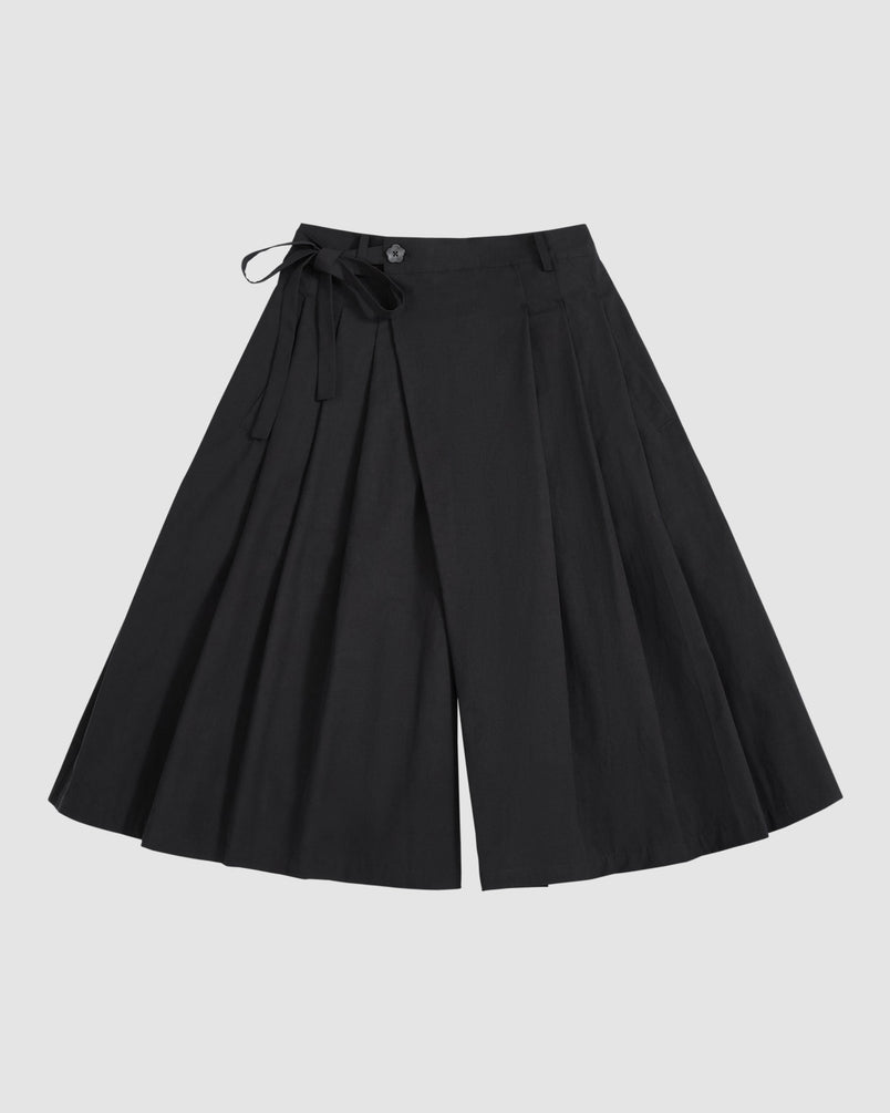 BLACK PLEATED HANBOK CULOTTES by Sundae School, featuring wide legs, pleats, a button closure, and a matching fabric tie at the waist, are displayed laid flat on a light gray background.