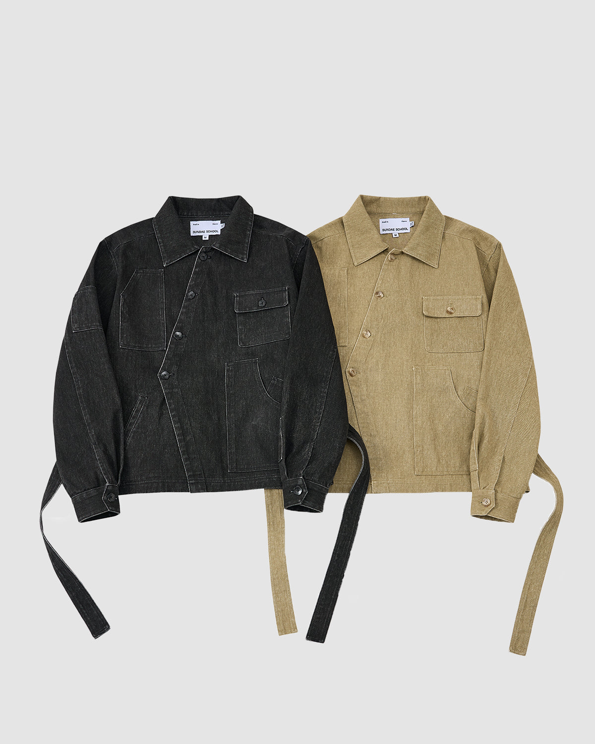 Two Sundae School TAN ASYMMETRIC WORK JACKETS, one in black and one in tan, each with seven pockets and long side straps, are laid flat on a white background.