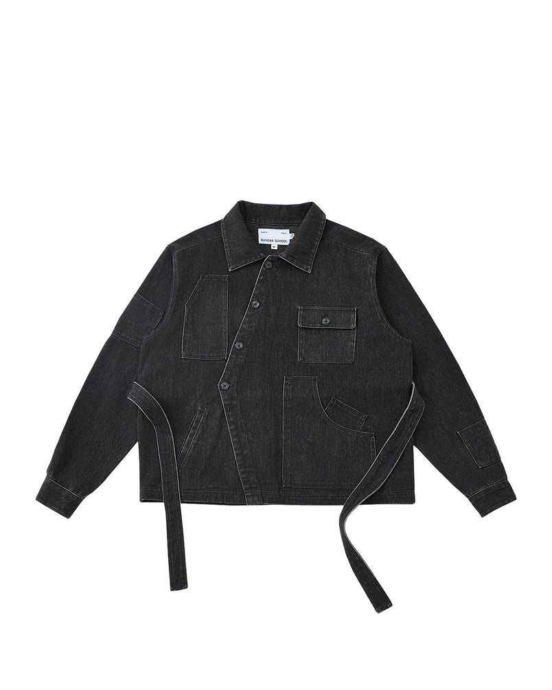 The BLACK ASYMMETRIC WORK JACKET by Sundae School is a black denim unisex piece with white stitching, button closure, long sleeves, pockets, and adjustable side fabric straps. Shown on a plain light gray background.