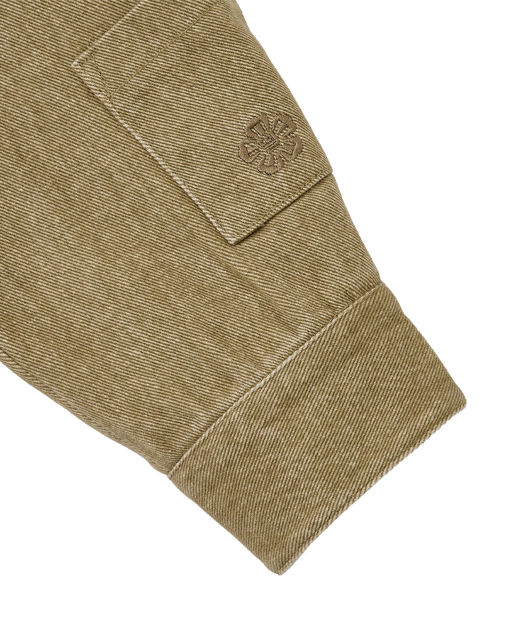 Close-up of the TAN ASYMMETRIC WORK JACKET by Sundae School shows its khaki sleeve, wide cuff, and stitched patch with an embossed circular emblem, highlighting the fabric's texture and quality craftsmanship.