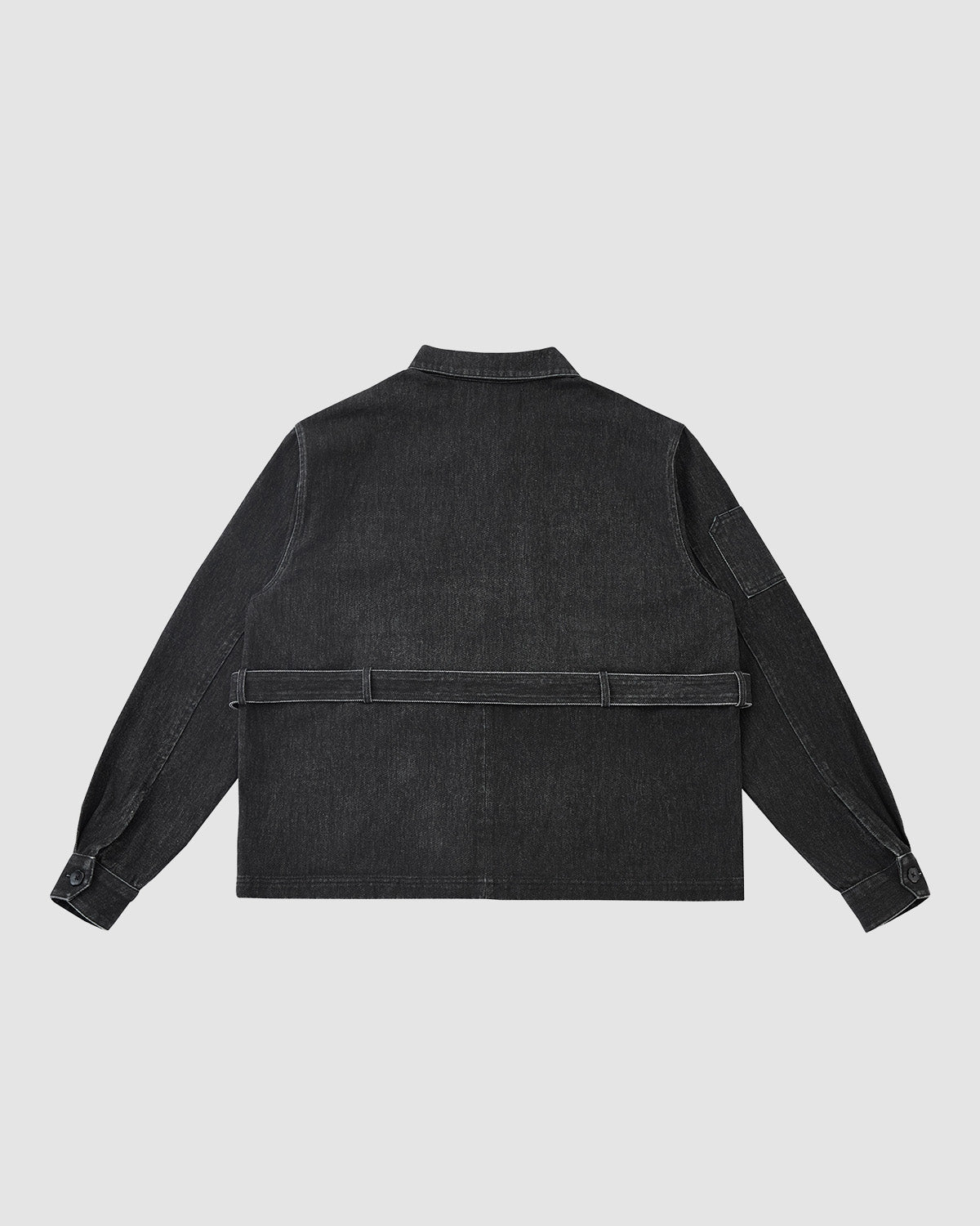 The BLACK ASYMMETRIC WORK JACKET by Sundae School is a unisex black denim jacket shown from the back with long sleeves, buttoned cuffs, practical pockets, a straight hem, and an asymmetric belt-like detail across the lower back.