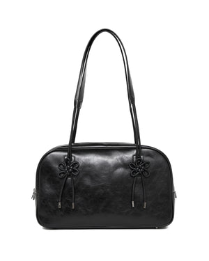 The BLACK AUDREY BOWLING BAG by Sundae School is a black leather handbag featuring two long handles and decorative knots on the front, displayed against a white background.