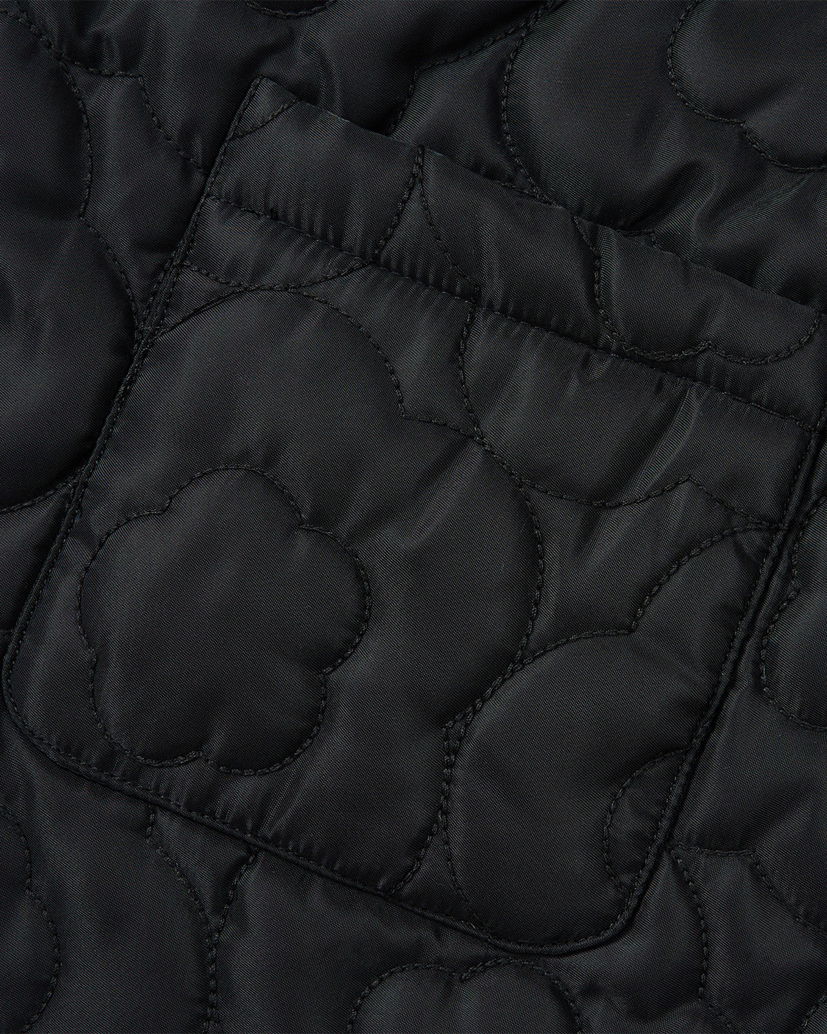 Close-up of the BLACK BAEJA VEST / BAG by Sundae School, showcasing black quilted fabric with a pocket and intricate stitching inspired by traditional Korean baeja designs. Floral and curved patterns create a textured, decorative surface.