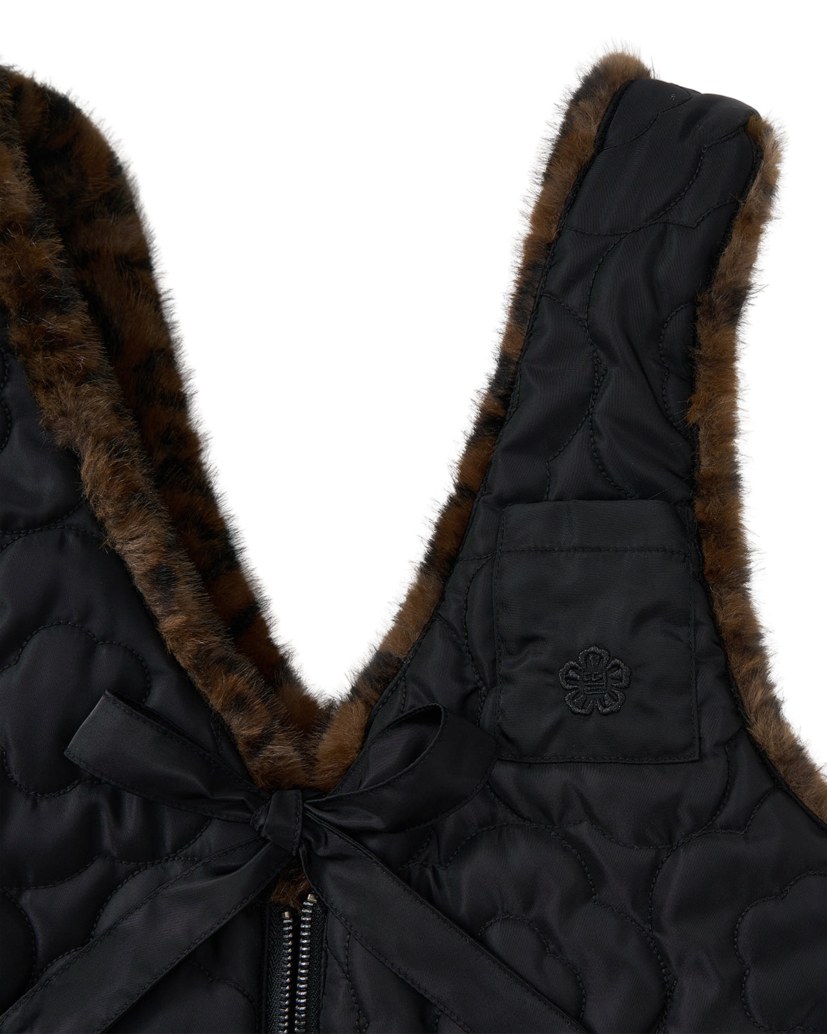 Close-up of the BLACK BAEJA VEST / BAG by Sundae School, a black quilted faux fur vest featuring a reversible design. The piece is detailed with a zipper closure, bow accent, and a stitched flower patch on the chest. Inspired by traditional Korean baeja styles, its elegant brown and black fur trim adds a distinctive touch.
