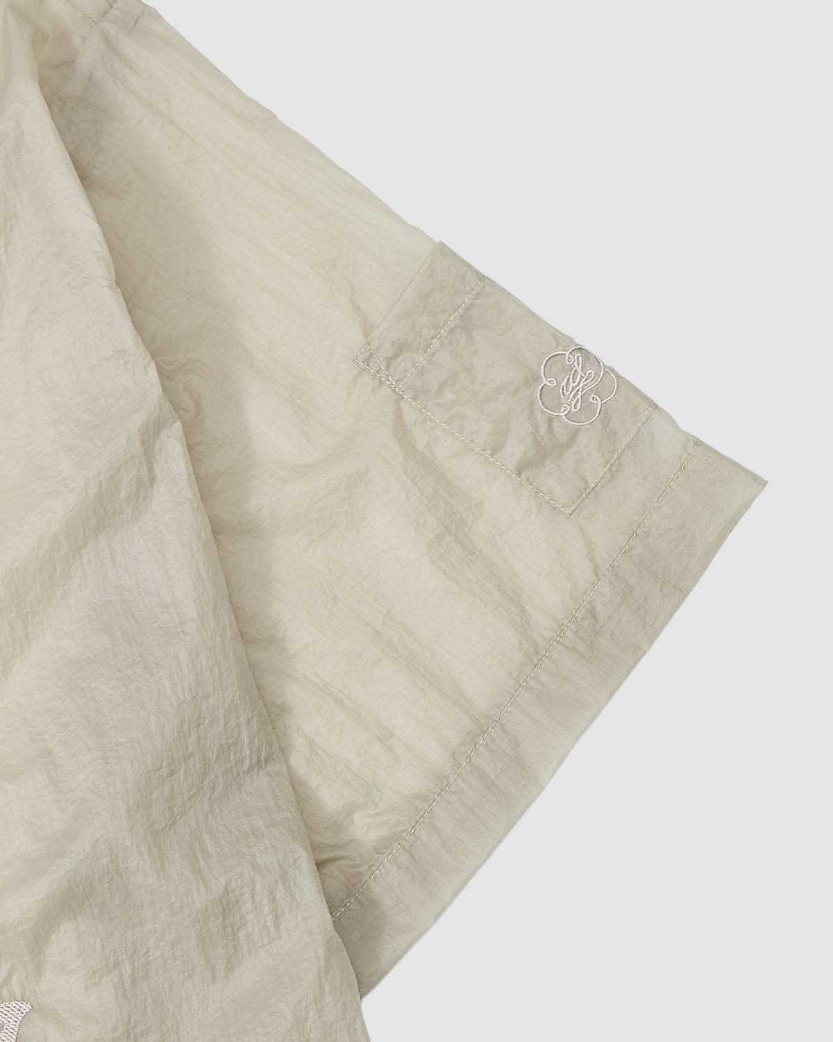 A close-up of the Sundae School BARONG SHIRT, a light beige, crinkled short-sleeve with a Filipino silhouette and a small white embroidered logo on the sleeve seam, shown against a plain background.