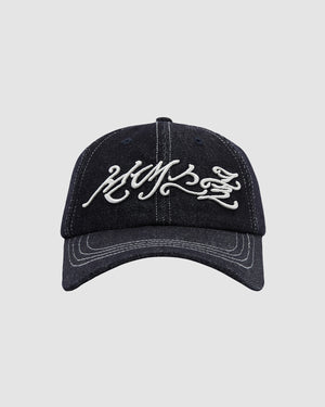 The INDIGO DAENGGI CAP by Sundae School is a black denim 6-panel cap with adjustable fit, white stylized script embroidery on the front, and crisp visible white stitching along the brim and panels.