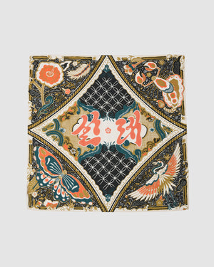 The MULTI-COLOR BATIK BANDANA by Sundae School is a square silk scarf featuring an intricate Indonesian batik-inspired pattern with flowers, a butterfly, and a crane in gold, black, teal, orange, and white around a central geometric diamond.