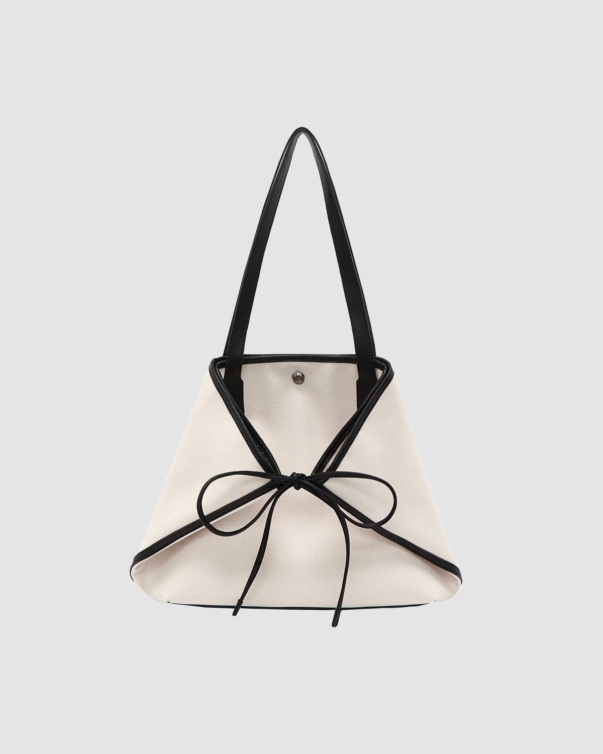 The Sundae School IVORY BOJAGI TIE TOTE BAG is a white trapezoid-shaped cotton canvas tote with black trim, shoulder straps, and a front bow detail, shown against a plain light gray background.
