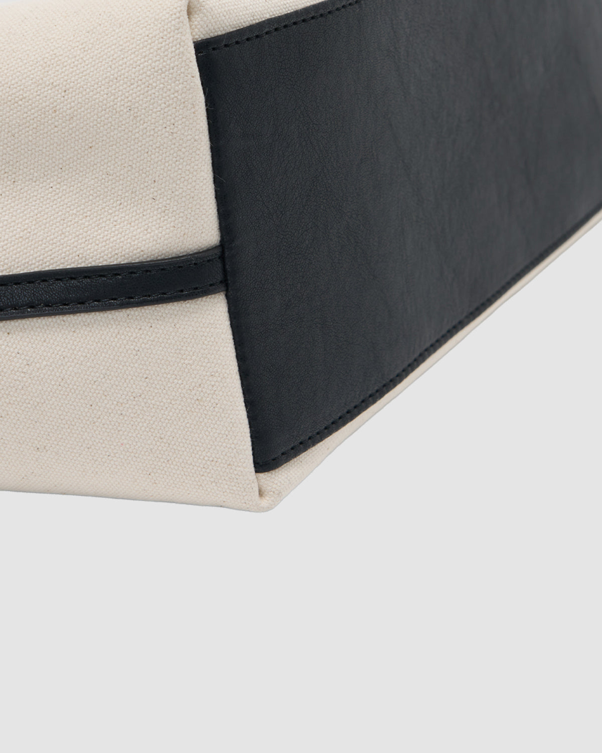 Close-up of the corner of the IVORY BOJAGI TIE TOTE BAG by Sundae School, crafted from beige cotton canvas and black vegan leather, highlighting its stitching and textured details.