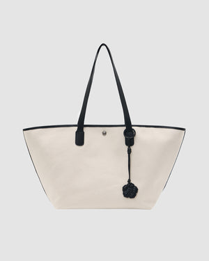 The IVORY BOJAGI TIE TOTE BAG by Sundae School is a spacious white vegan leather tote with black handles, black trim, and a decorative charm, shown against a plain light gray background.