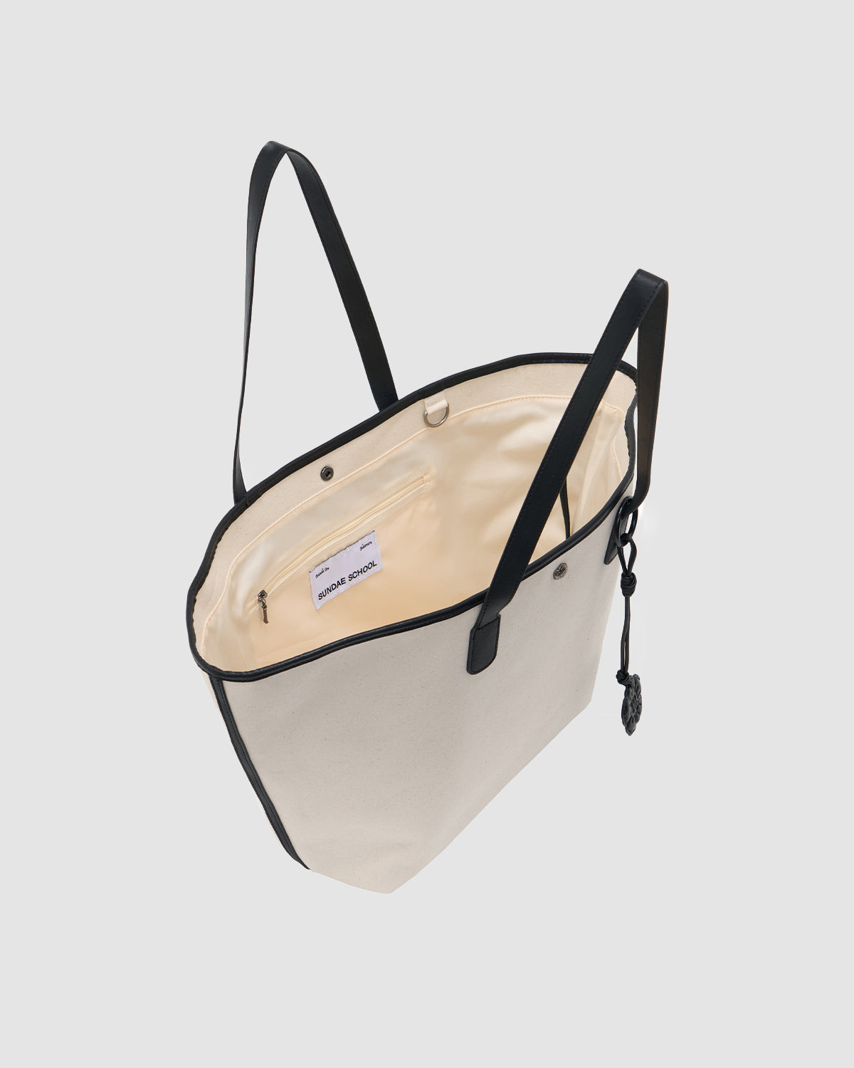 The IVORY BOJAGI TIE TOTE BAG by Sundae School is a chic cream cotton canvas tote with black handles and trim, featuring a light interior, zippered pocket, and small label—spacious and stylish for everyday use.
