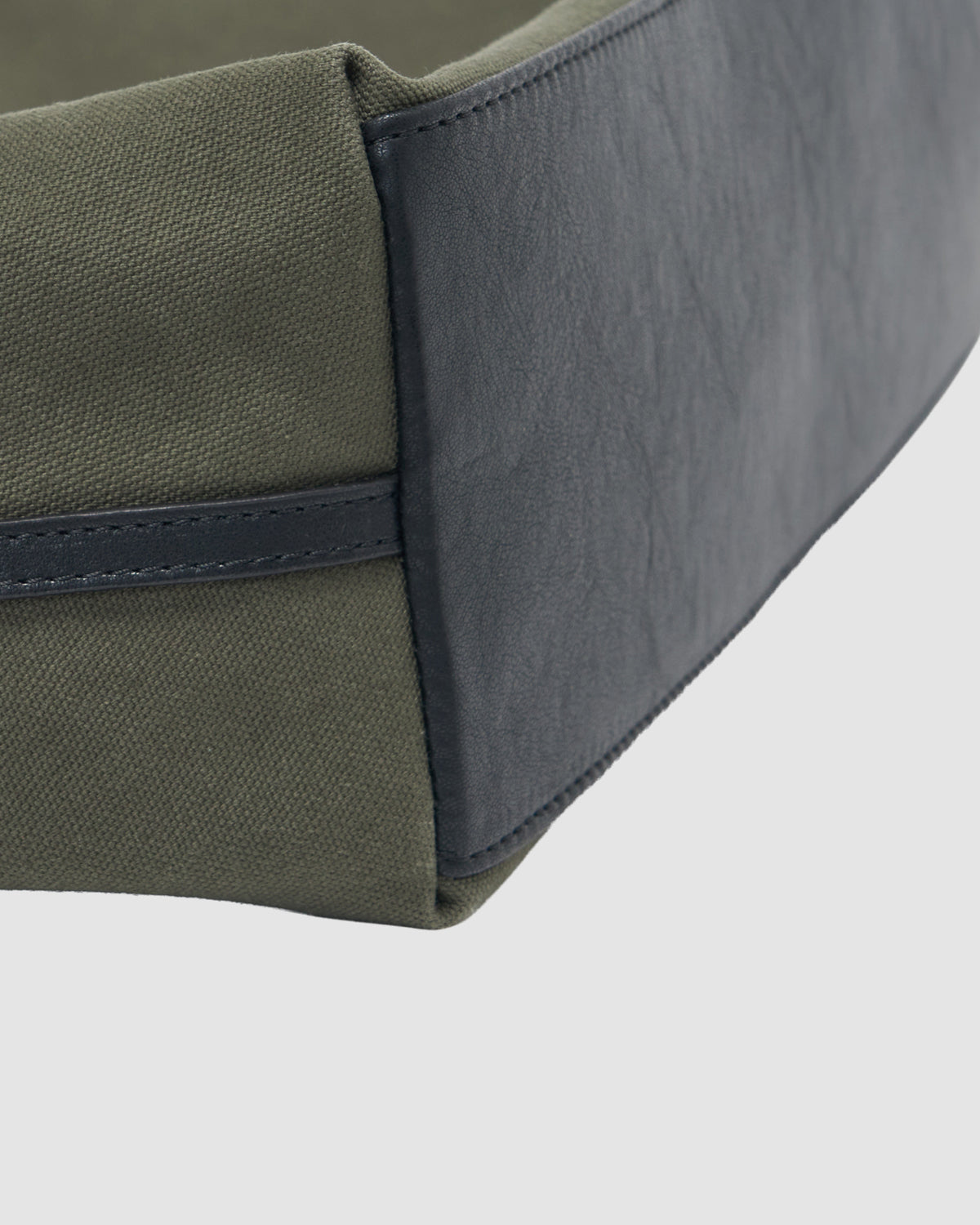 Close-up of the corner of the Sundae School OLIVE BOJAGI TIE TOTE BAG, featuring green canvas sides and a dark gray vegan leather trim against a plain light background.