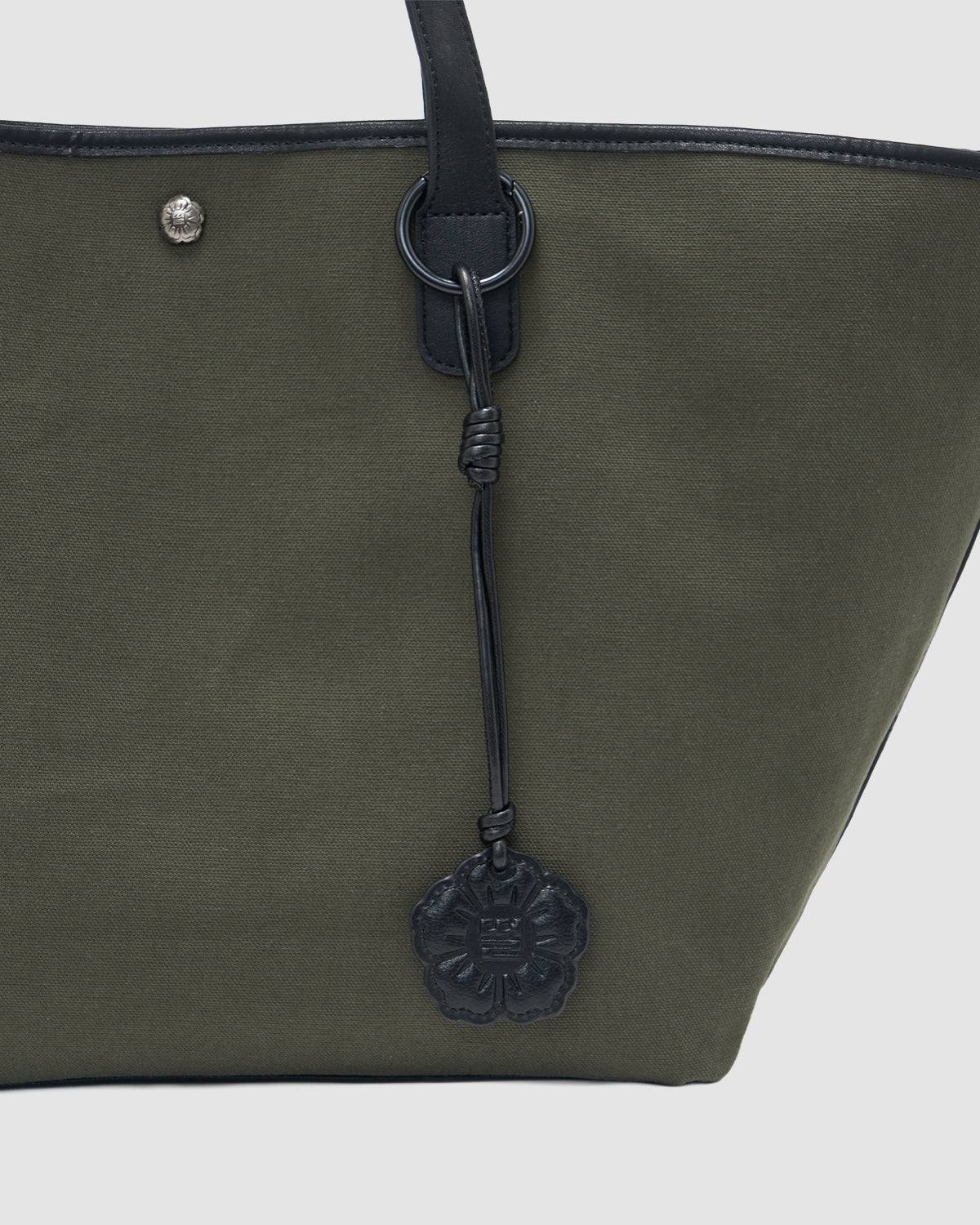 A close-up of the Sundae School OLIVE BOJAGI TIE TOTE BAG featuring black vegan leather trim handles, a black flower-shaped charm, and a small round metal accent near the top.
