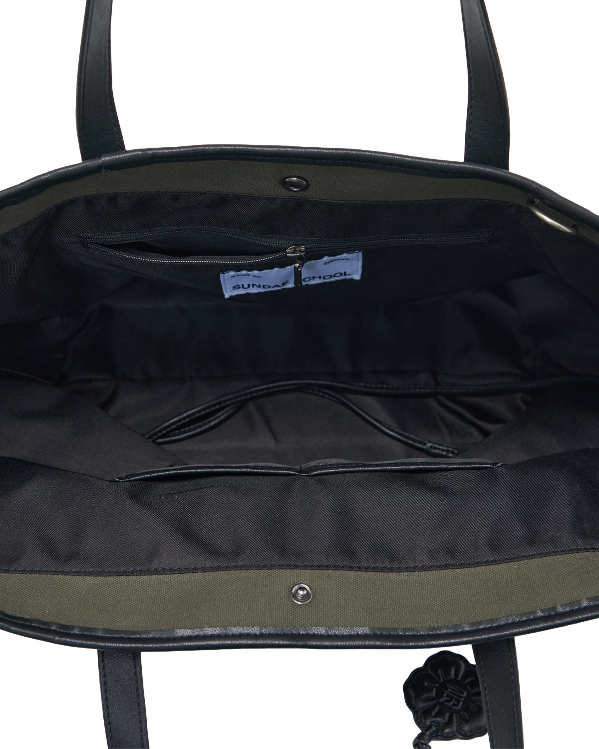 The OLIVE BOJAGI TIE TOTE BAG by Sundae School is shown open in black vegan leather, revealing a spacious interior with fabric lining, a zippered pocket, and a visible label inside. The bag features two handles and a top metal snap closure.