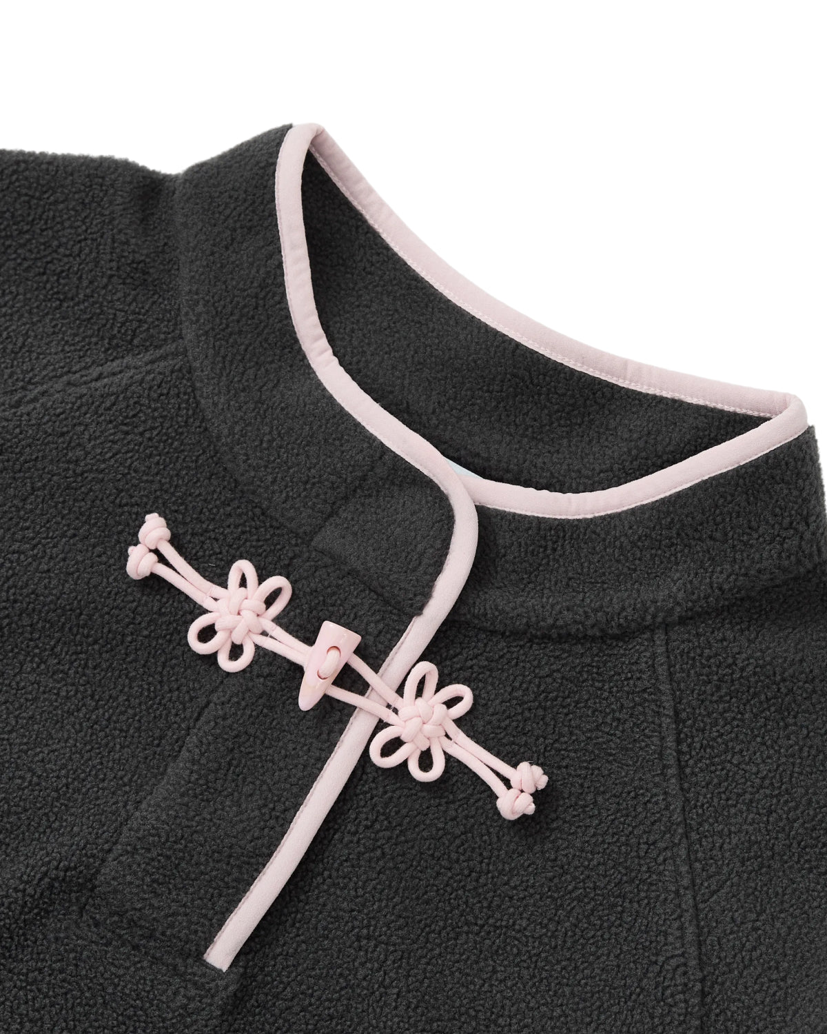Close-up of the CHARCOAL BUTTERFLY FLEECE PULLOVER by Sundae School, a dark grey mock-neck polar fleece with light pink trim and a decorative pink frog button clasp at the collar, featuring intricate hand-tied flower knots.