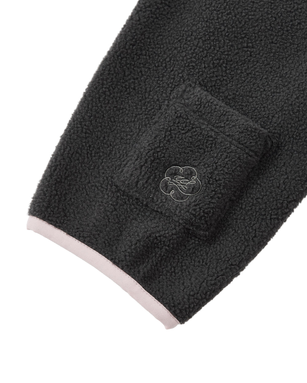 A close-up of the CHARCOAL BUTTERFLY FLEECE PULLOVER by Sundae School reveals a black fleece sleeve with a small embroidered pocket and a pink edge at the cuff, highlighting the unique tteokbokki toggles featured on this mock-neck polar fleece pullover.