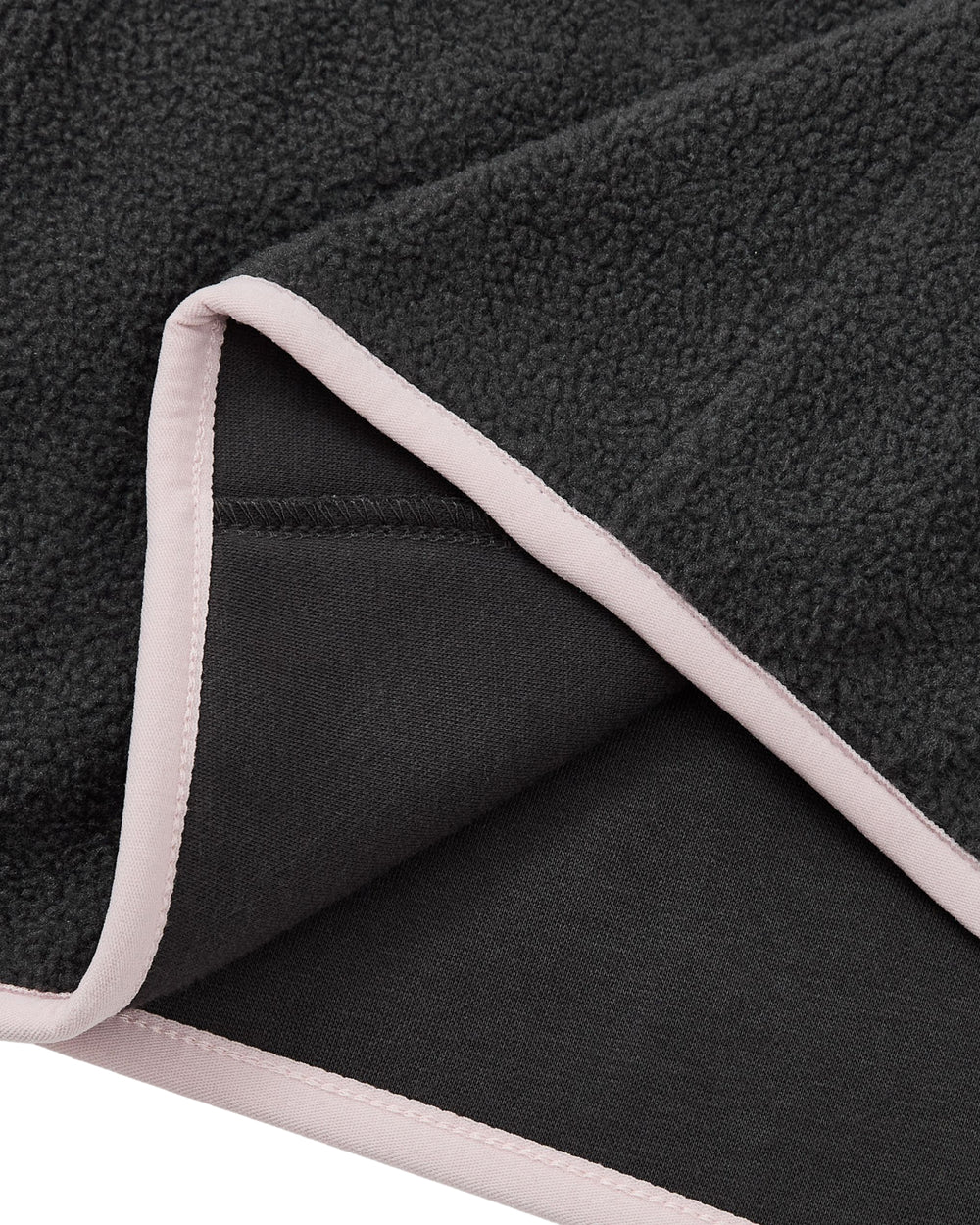 A close-up of the Sundae School CHARCOAL BUTTERFLY FLEECE PULLOVER showcases its soft, textured black fleece fabric with light pink trim along the edges, partially folded to reveal both sides and finished with delicate hand-tied flower knots at the corners.