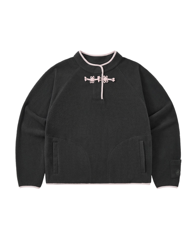 The CHARCOAL BUTTERFLY FLEECE PULLOVER by Sundae School is a black polar fleece sweater with light pink trim, featuring a mandarin collar adorned with decorative hand-tied flower knots at the neck. This mock-neck pullover offers two front pockets and a relaxed, casual fit.