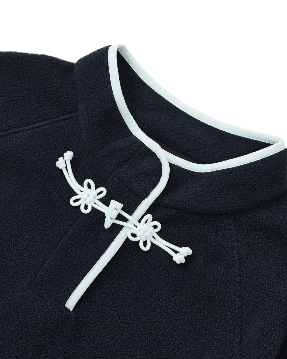 Close-up of the NAVY BUTTERFLY FLEECE PULLOVER by Sundae School, a navy blue polar fleece pullover detailed with white trim and a frog button closure at the collar, featuring decorative flower knot toggles.