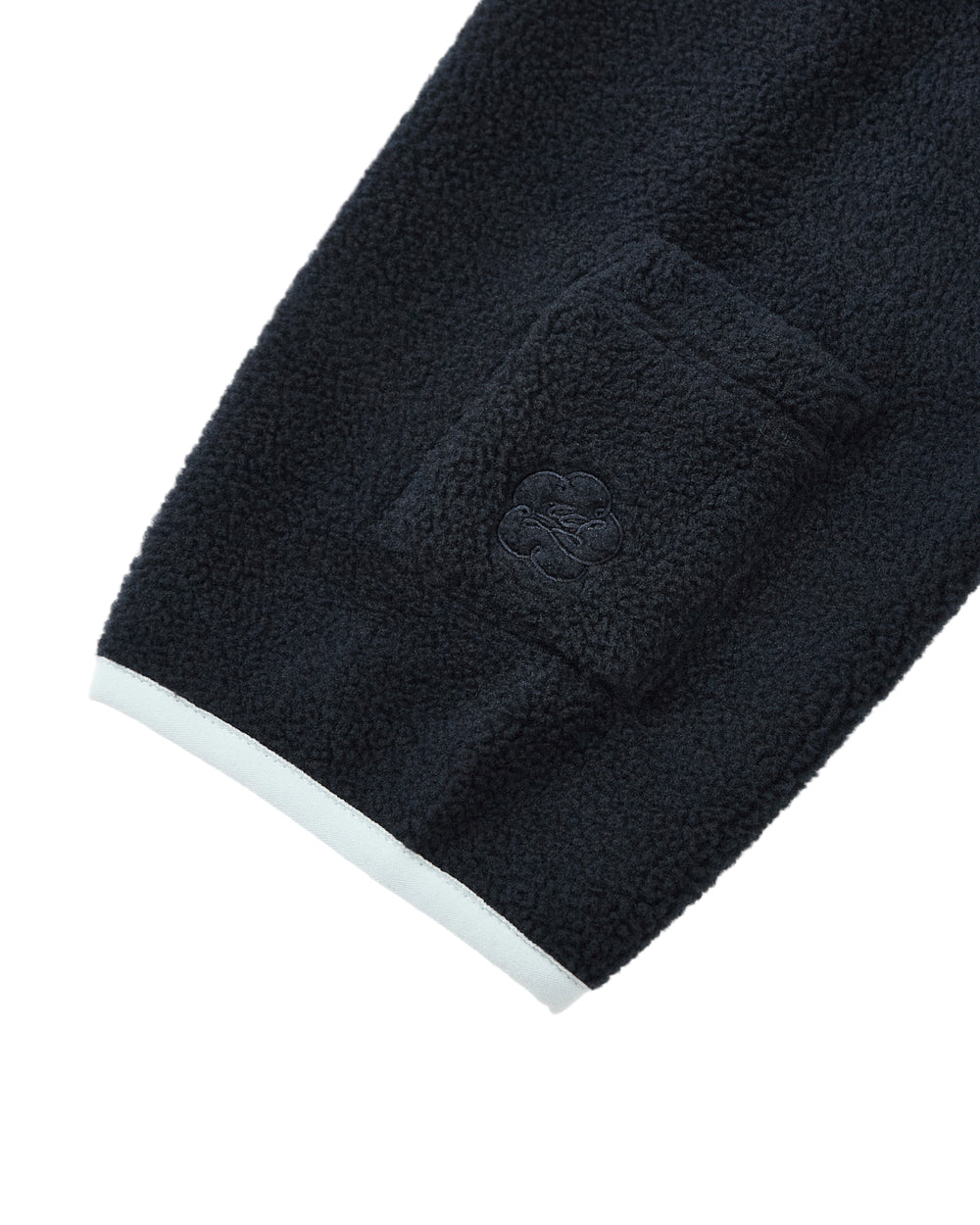 A close-up of the NAVY BUTTERFLY FLEECE PULLOVER by Sundae School showcases its navy blue polar fleece sleeve featuring a small, rectangular pocket and an embroidered logo near the cuff, which is finished with a crisp white trim. Subtle flower knot toggles add a unique accent to the design.