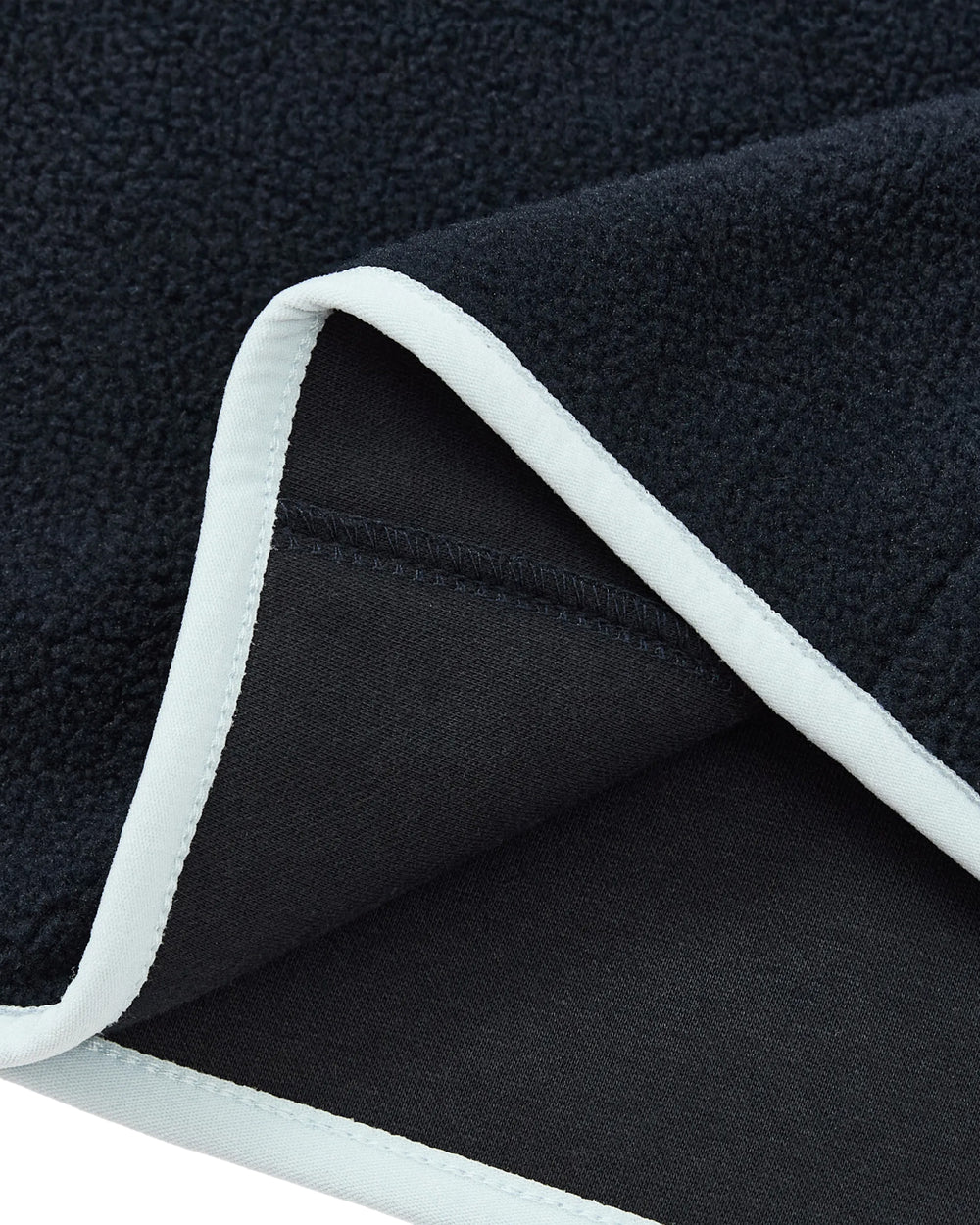A close-up of Sundae School’s NAVY BUTTERFLY FLEECE PULLOVER reveals its dark, plush fleece fabric edged with crisp white trim, highlighting both the soft, textured surface and the smooth underside—evoking the cozy feel of a classic pullover—with one corner stylishly folded over.