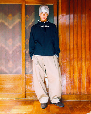A person with short gray hair wears the Sundae School NAVY BUTTERFLY FLEECE PULLOVER and baggy beige pants, standing indoors against wooden sliding doors.