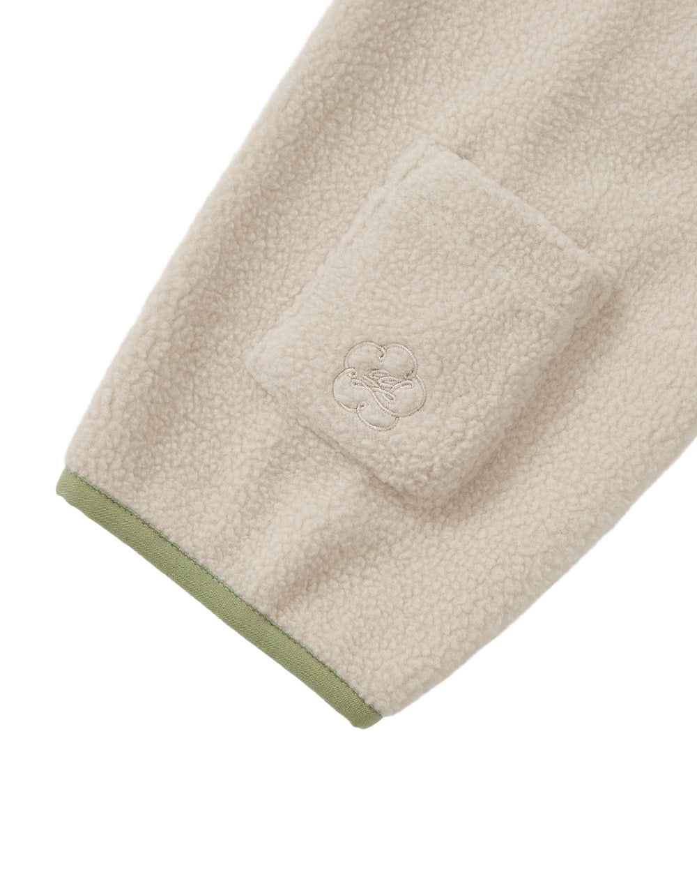 A close-up of the Sundae School TAUPE BUTTERFLY FLEECE PULLOVER shows a cream-colored mock-neck polar fleece sleeve featuring a small pocket and an embroidered flower motif. The cuff is trimmed with light green fabric, while hand-tied flower knots provide a charming finishing touch.