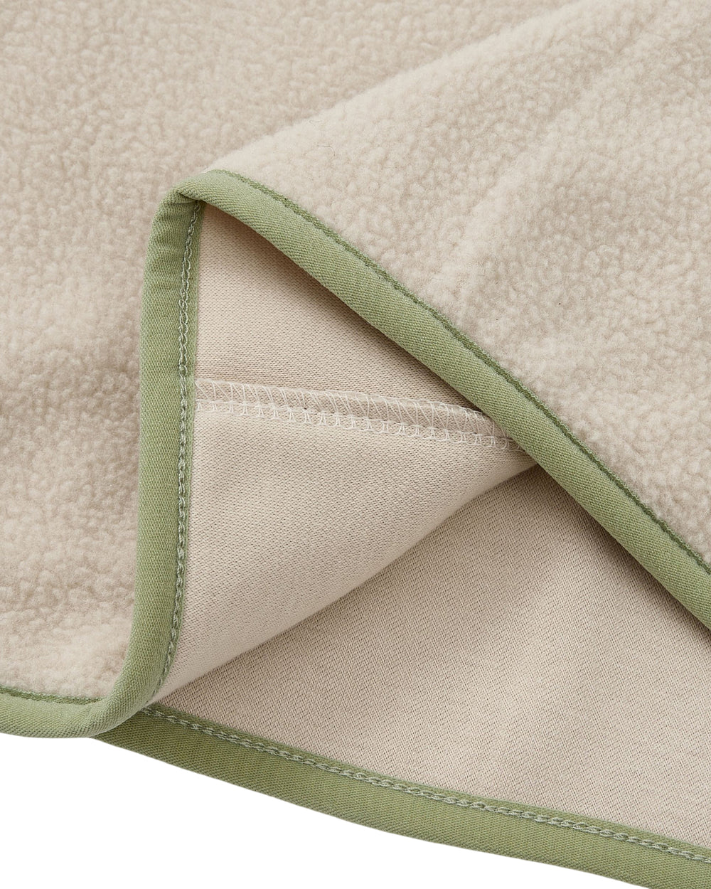 A close-up of the TAUPE BUTTERFLY FLEECE PULLOVER by Sundae School highlights its beige, soft, and textured surface with delicate light green trim along the edges. The corner of the pullover is folded to reveal both sides, evoking the cozy comfort typical of a mock-neck polar fleece blanket. Subtle hand-tied flower knots add an elegant touch to its design.
