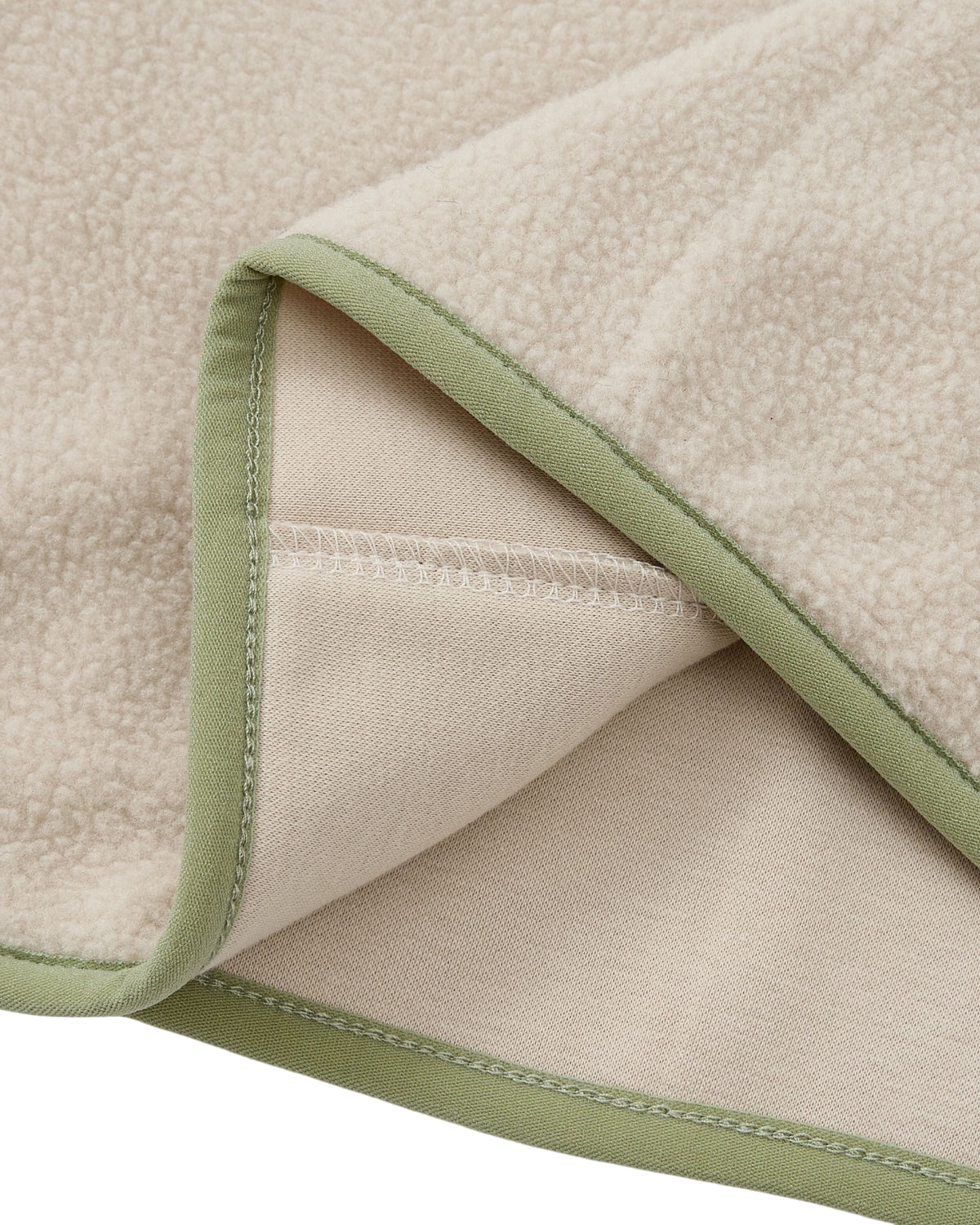 A close-up of the TAUPE BUTTERFLY FLEECE PULLOVER by Sundae School highlights its beige, soft, and textured surface with delicate light green trim along the edges. The corner of the pullover is folded to reveal both sides, evoking the cozy comfort typical of a mock-neck polar fleece blanket. Subtle hand-tied flower knots add an elegant touch to its design.