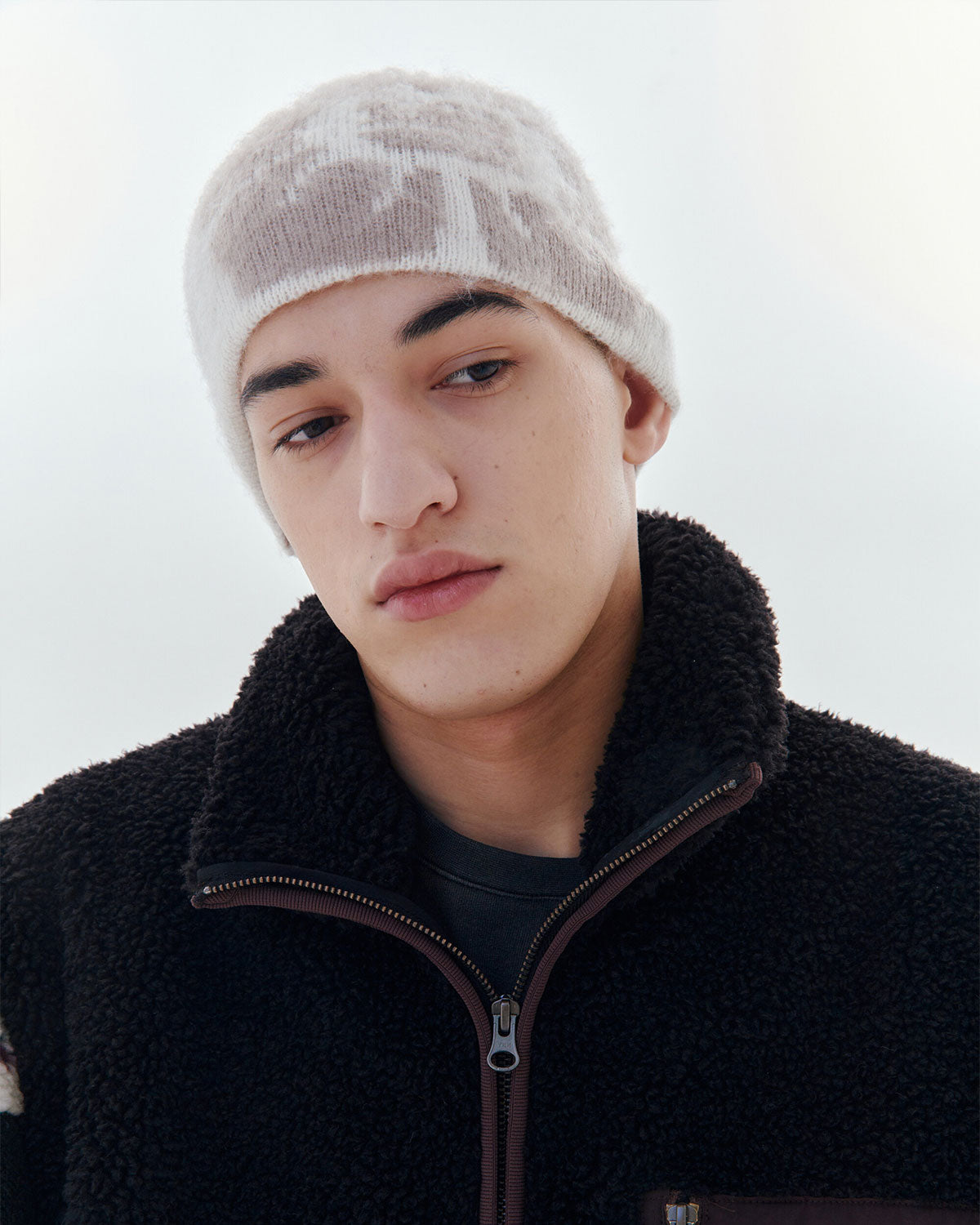 A young person wears the Sundae School Ivory Ddul Beanie and a black fleece zip-up, looking down calmly—subtly prioritizing brain protection and safety against a light background.