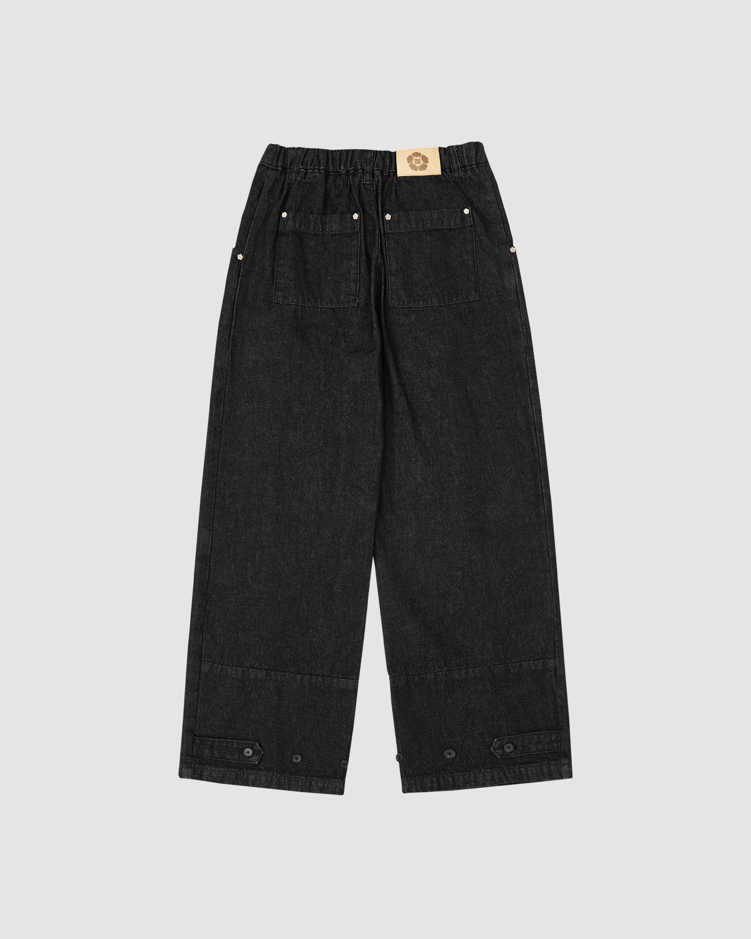 Back view flat lay of Sundae School black wide-leg hanbok denim pants showing elastic waistband, tan leather brand patch with flower logo, back pockets with silver snap button details, and wide-leg silhouette