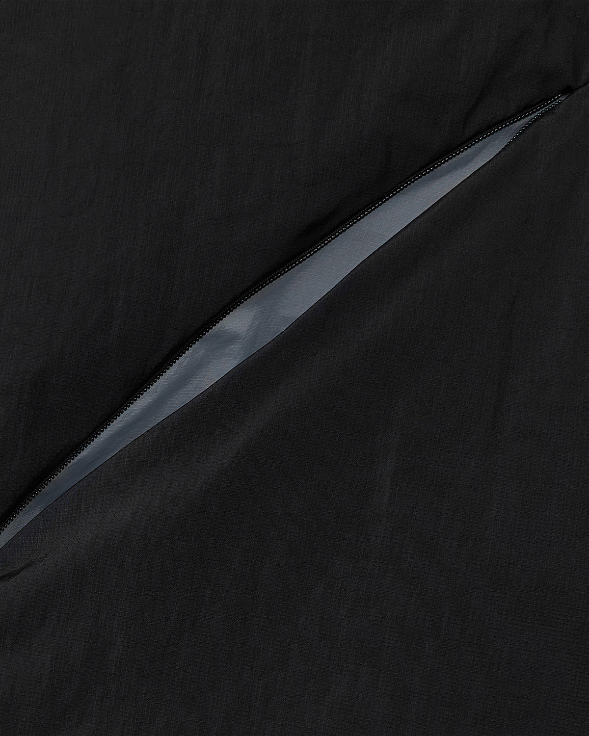 A close-up of the diagonal zippered pocket on the BLACK SKY BLUE ORIGAMI PUFFER by Sundae School, showing black fabric with a partially open zipper that reveals the lining inside.