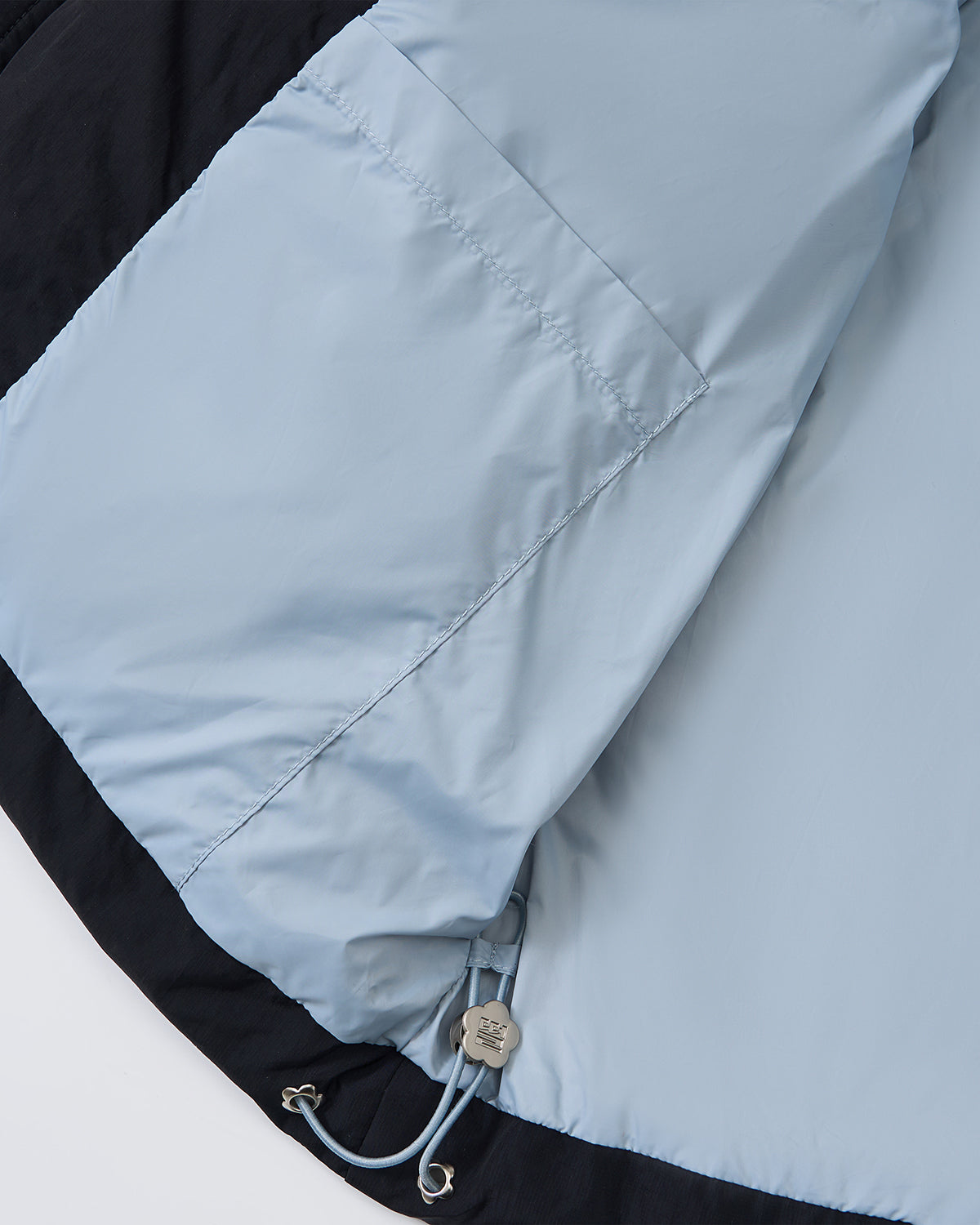 A close-up of the BLACK SKY BLUE ORIGAMI PUFFER by Sundae School highlights a large inner pocket, drawstring with metal toggles, and part of the jacket lining.