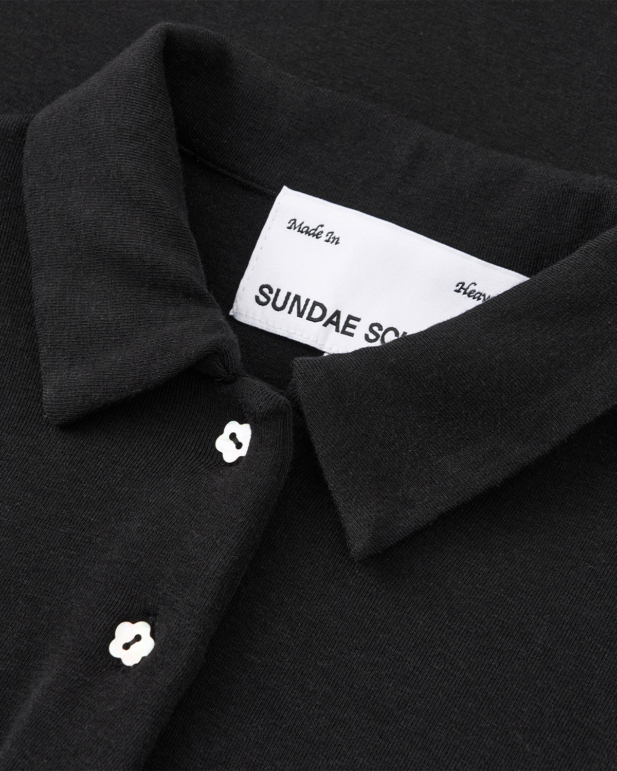 Close-up of the CINDY POLO DRESS by Sundae School, a black collared dress with white flower-shaped buttons and a 