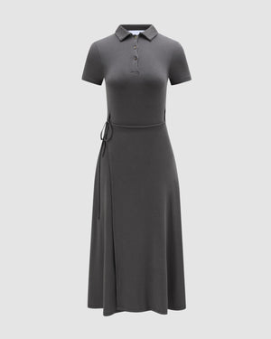 The DARK GREY CINDY POLO DRESS by Sundae School is a short-sleeve, dark gray polo dress with a buttoned collar and waist tie, showcasing a fitted midi silhouette, displayed on a plain light background.