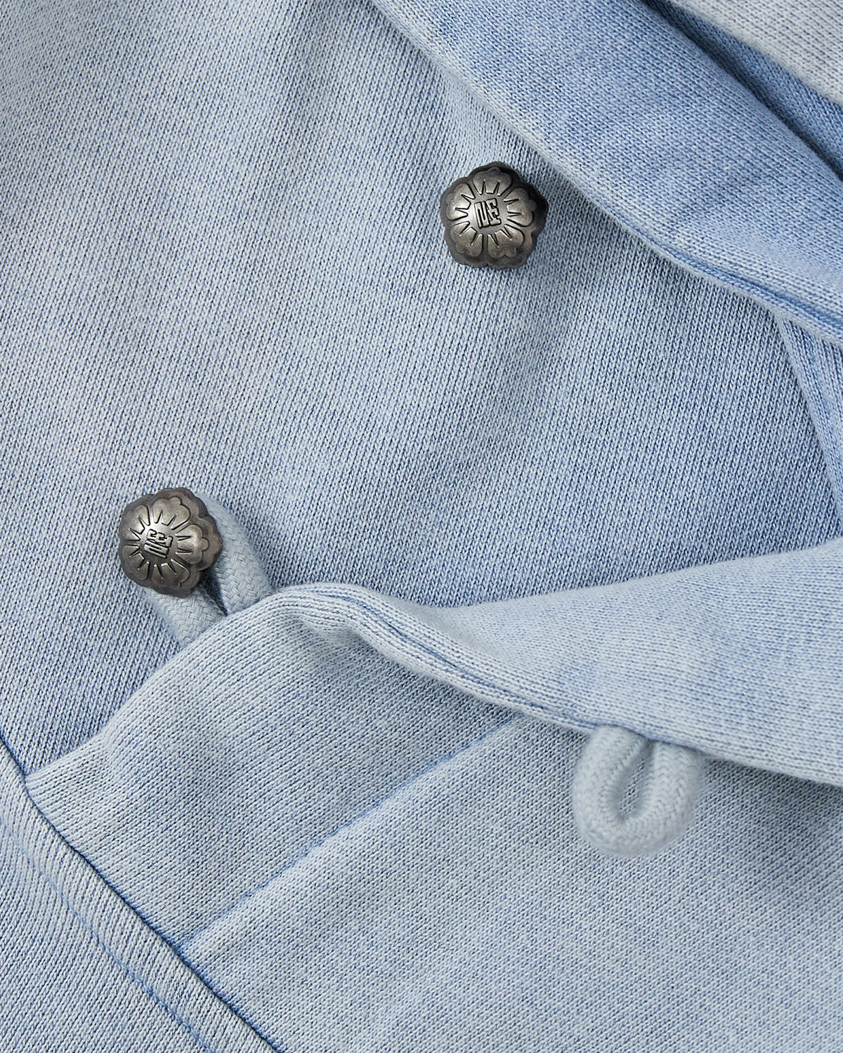 Close-up of the SKY BLUE COCOON HOODIE by Sundae School, featuring silver floral-engraved buttons, fabric loops, and detailed stitching—perfect for cocoon-core outfits or pieces with peret sleeves.