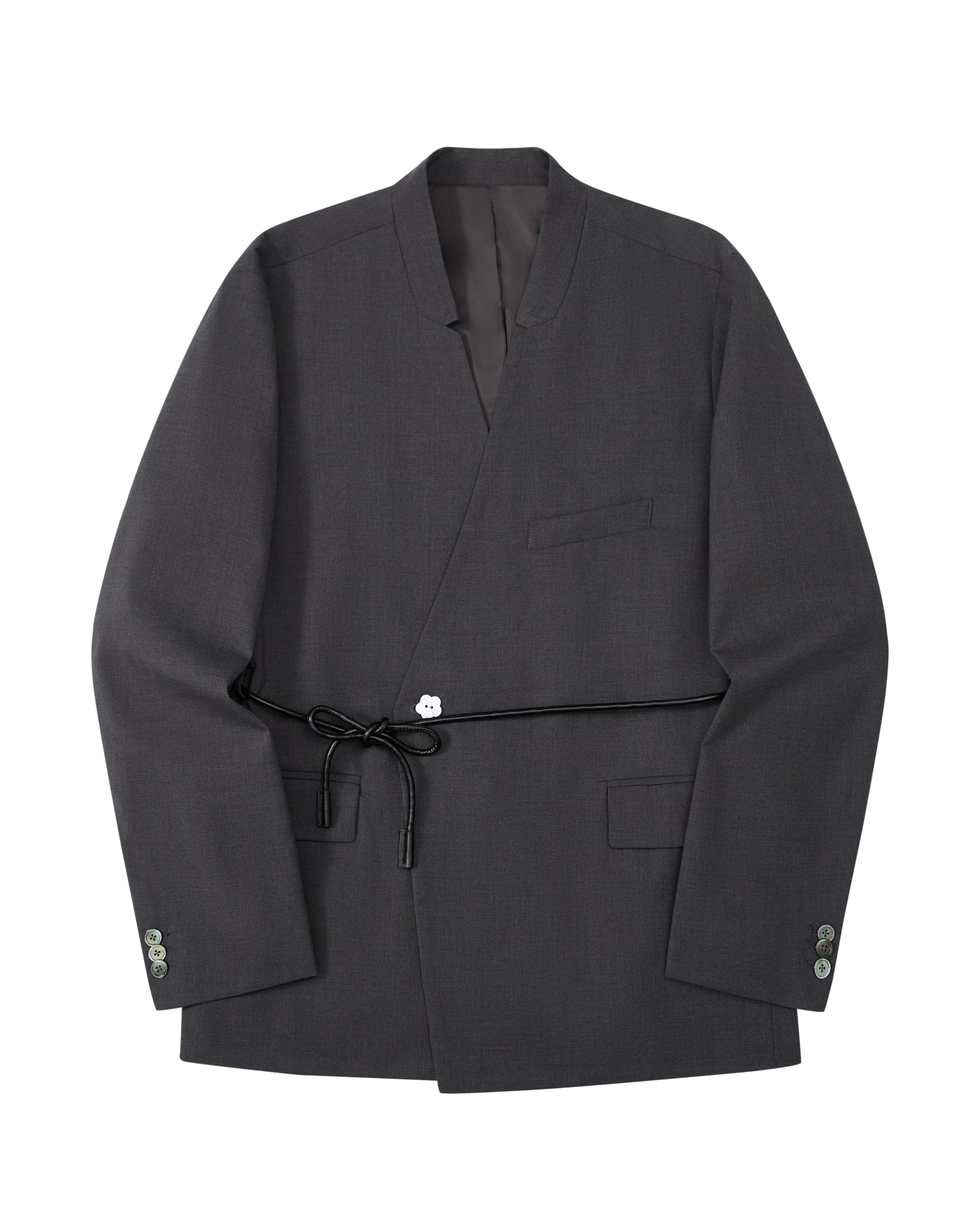 The COLLARLESS TIE BLAZER by Sundae School is a dark gray blazer with an unstructured drape and a shawl collar, designed without buttons. It features a single chest pocket, two front flap pockets, and comes with a thin vegan leather belt that ties at the waist.