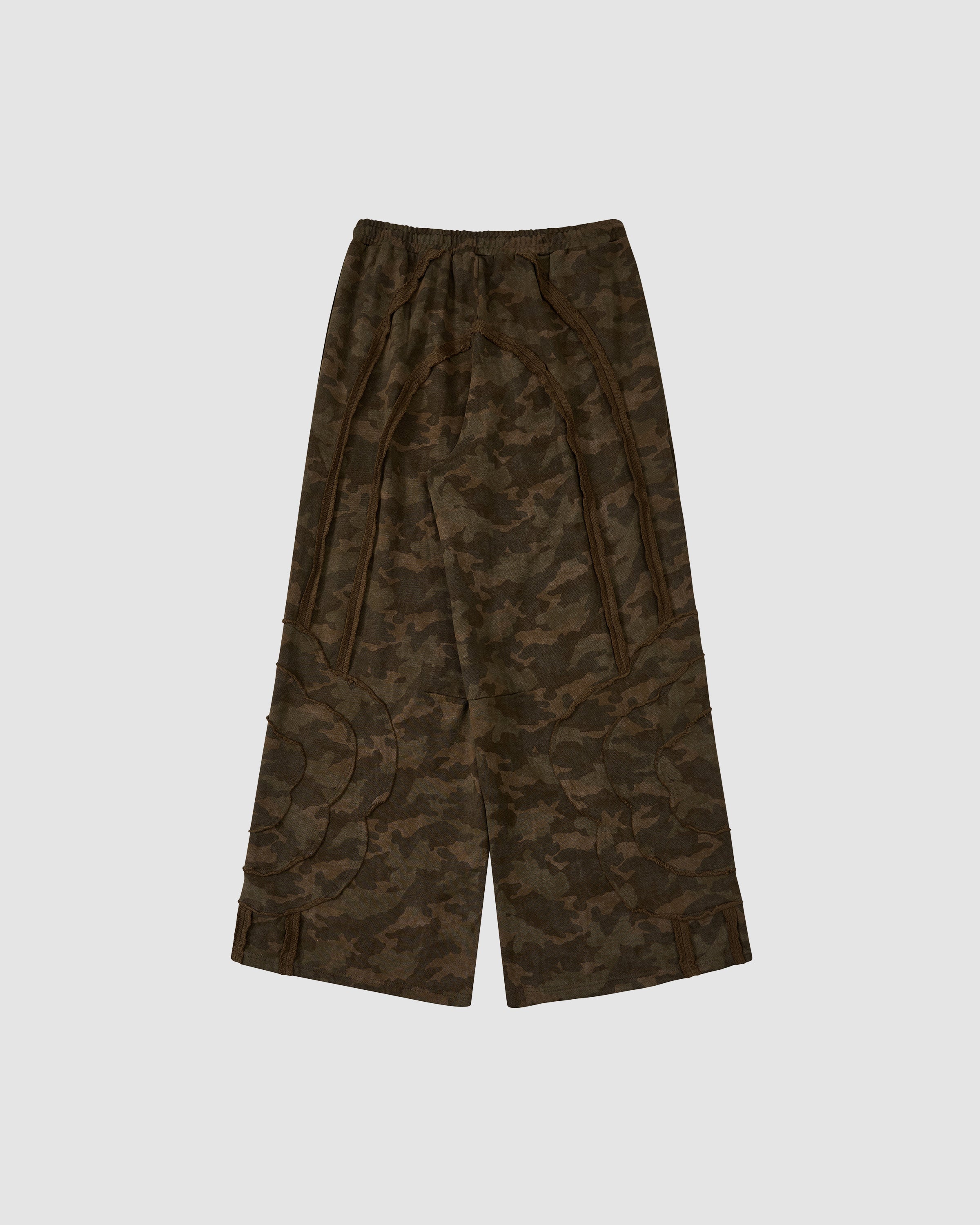 The CAMO MOCHI HAZE PANELED SWEATPANTS by Sundae School are wide-leg camo pants in brown and green 100% cotton with stitched patterns and an elastic waistband, shown against a plain light gray background.